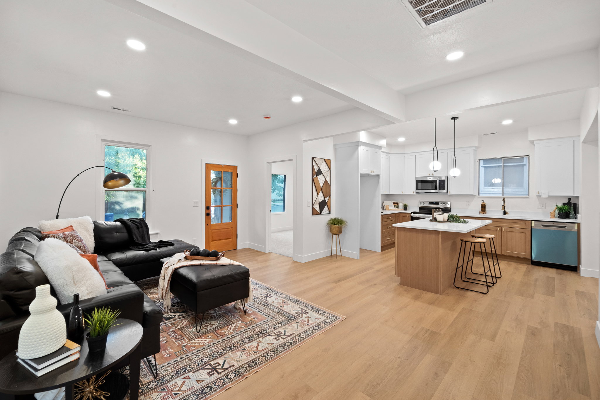 Open-concept living area featuring light wood-finish flooring, recessed lighting, a kitchen island with pendant lighting, white cabinetry, and stainless steel appliances