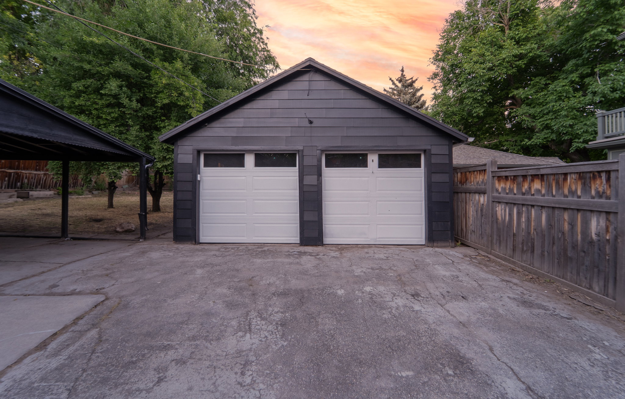 Two-car garage with white paneled doors and upper window inserts, featuring dark gray horizontal siding