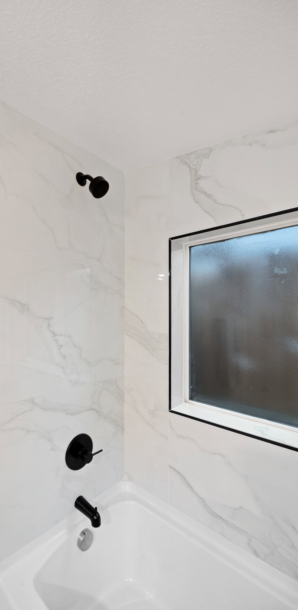 Bathtub with matte black fixtures and a window with black trim