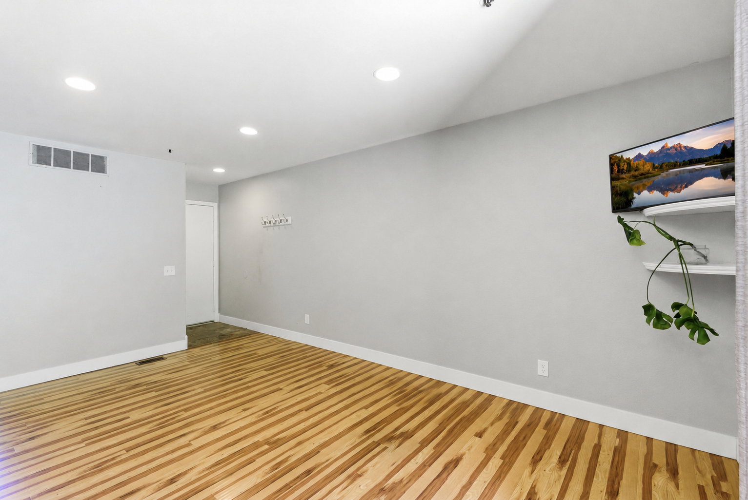 Spacious room featuring light wood-finish flooring, recessed ceiling lighting, a wall-mounted coat rack, and white baseboards
