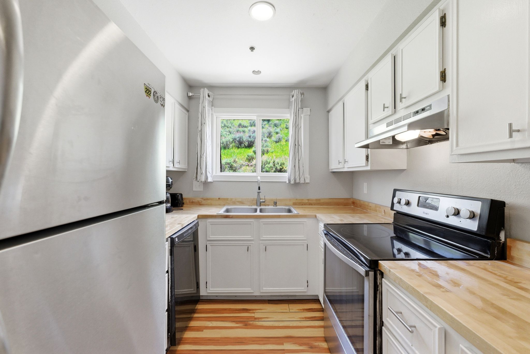Kitchen featuring bright white cabinetry, wood-finish countertops, stainless steel refrigerator, black electric range, and a dual basin sink