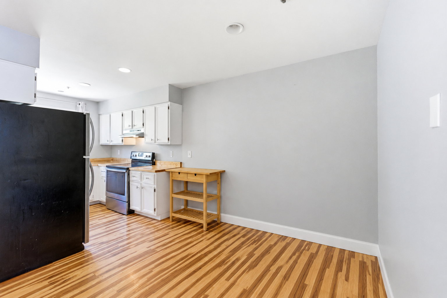 Kitchen featuring wood-finish flooring, white cabinetry, light countertops, and stainless steel appliances