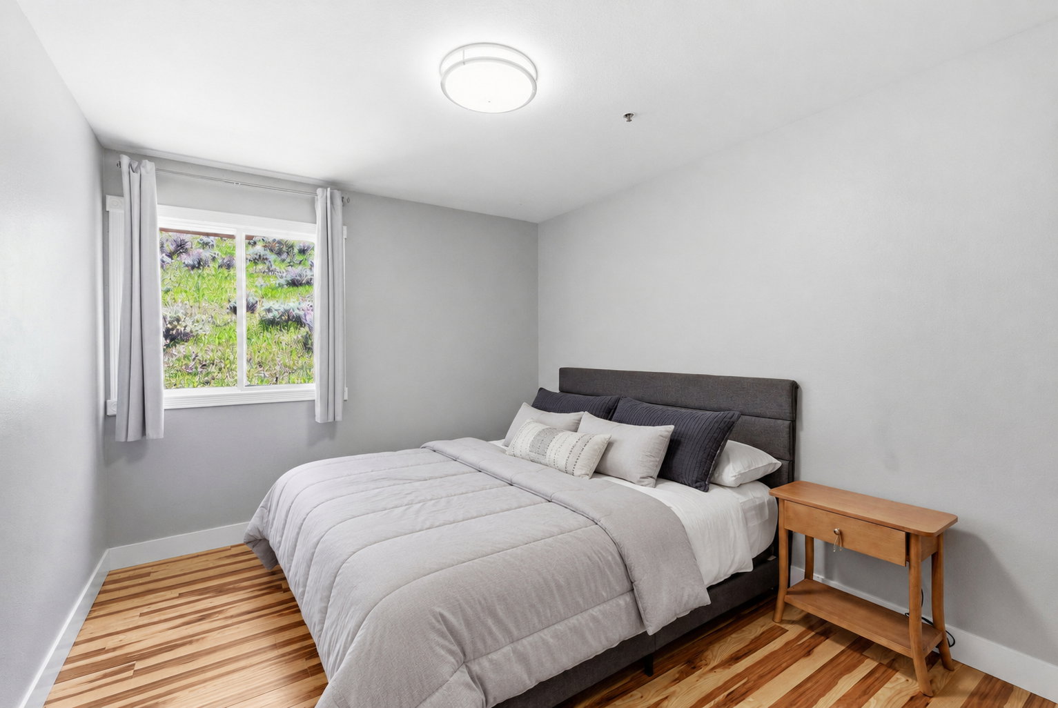 Bright interior space featuring wood-finish flooring, a single window with white trim, and a flush-mount ceiling light fixture