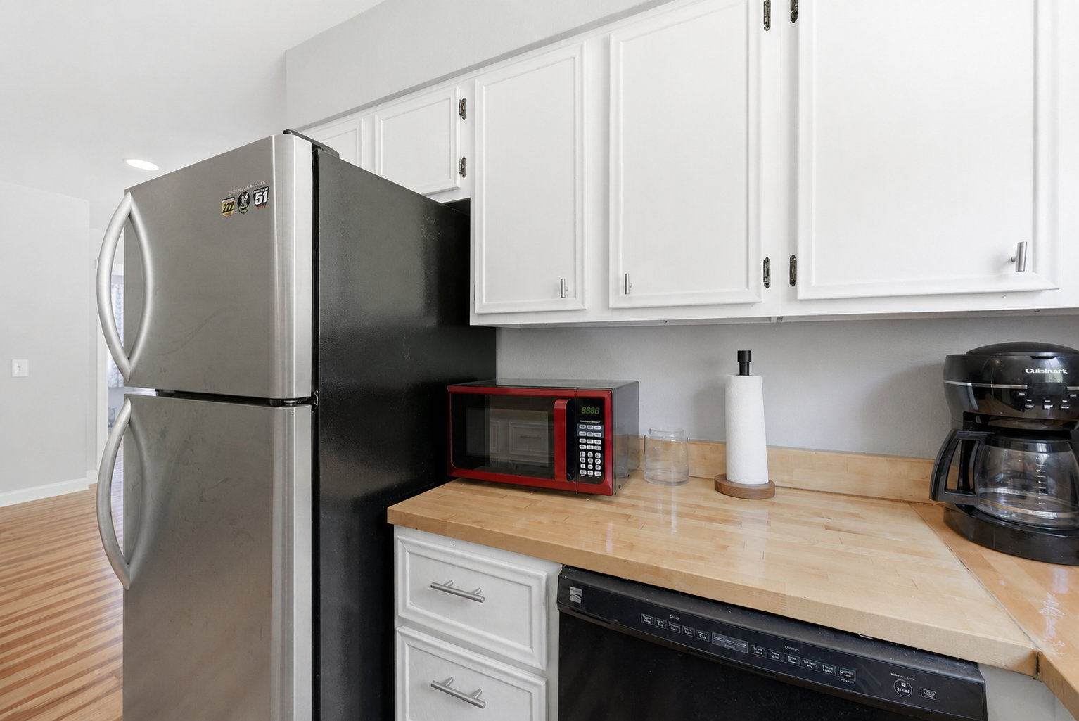 Stainless steel refrigerator, white upper cabinetry, wood-finish countertops, and a built-in dishwasher