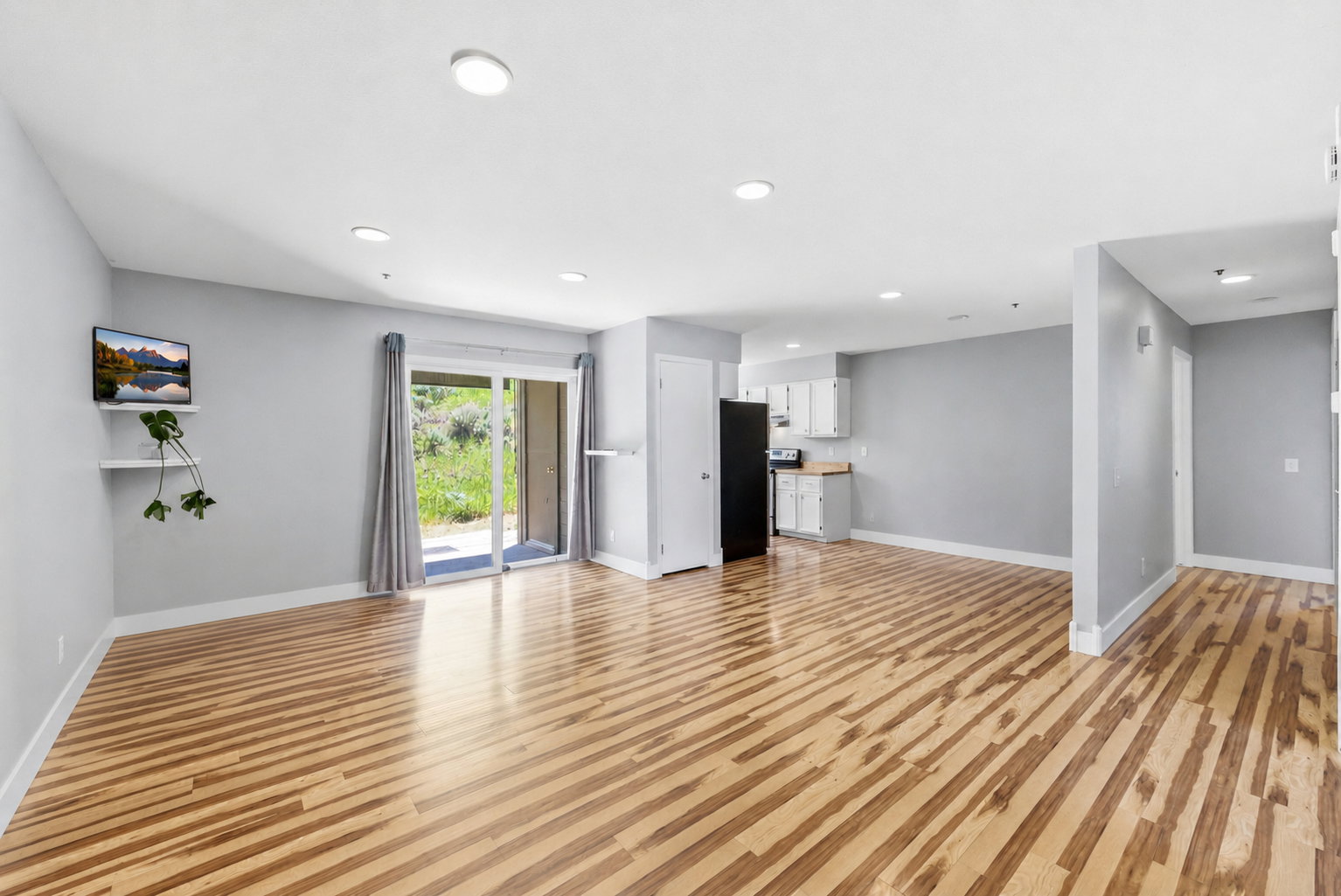 Spacious open-concept living area featuring wood-finish flooring, recessed lighting, and a sliding glass door