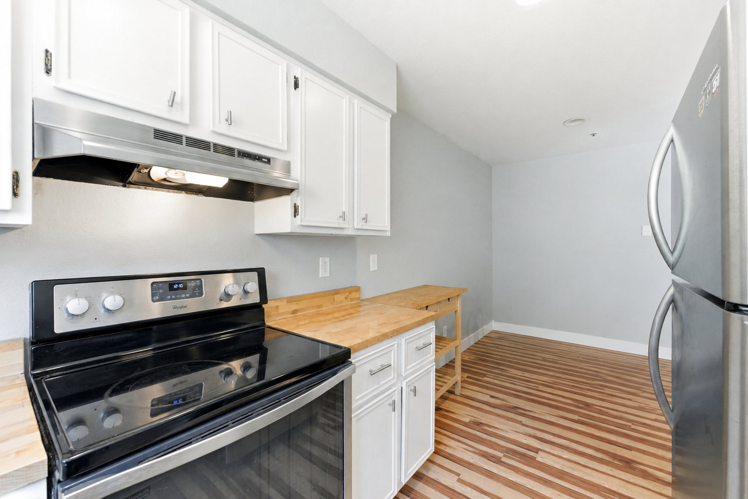 Kitchen featuring white cabinetry, wood-finish countertops, stainless steel appliances, and wood-finish flooring