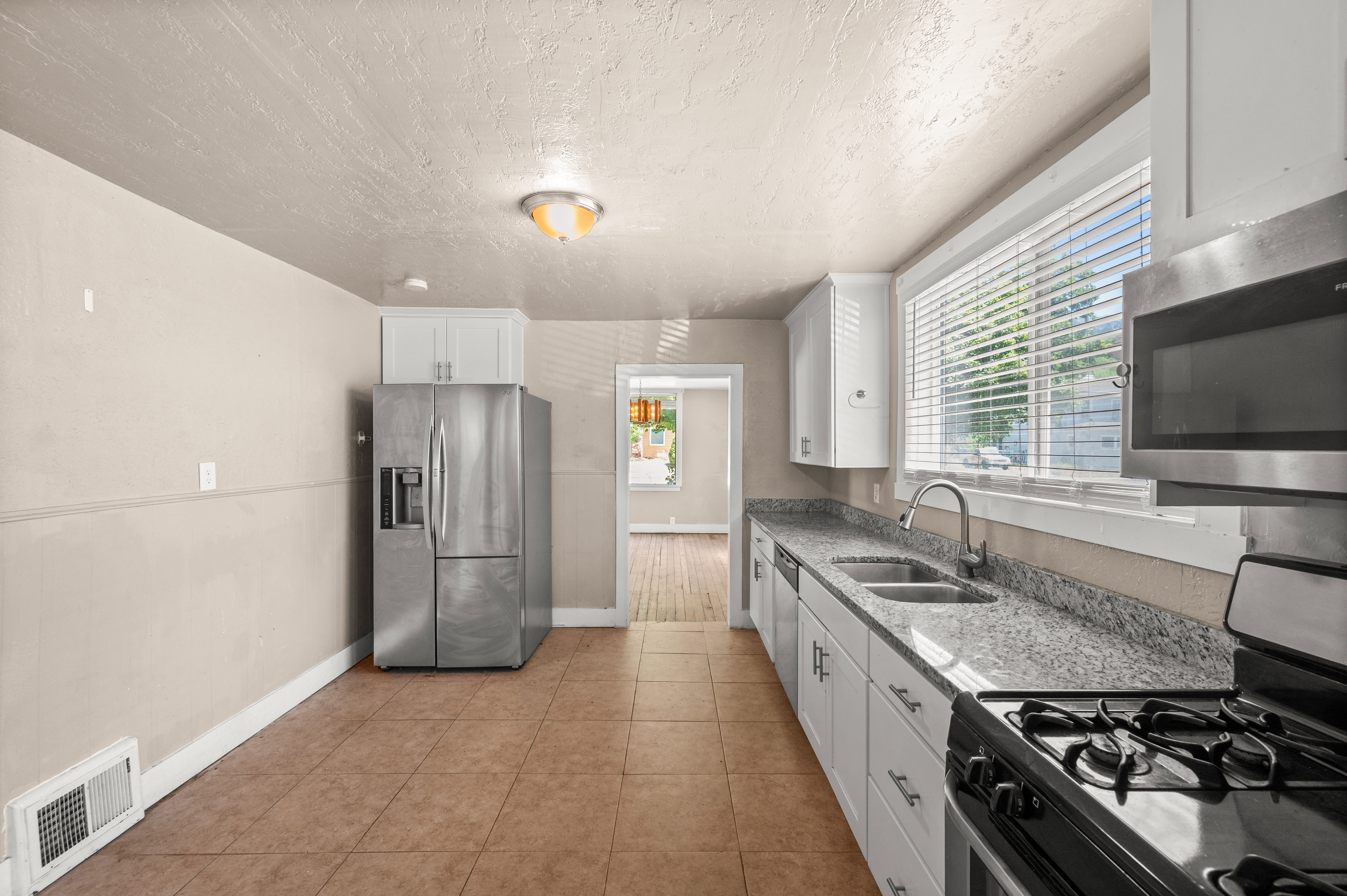 Kitchen featuring tile flooring, white cabinetry, a dual basin sink, a gas range, and a stainless steel microwave