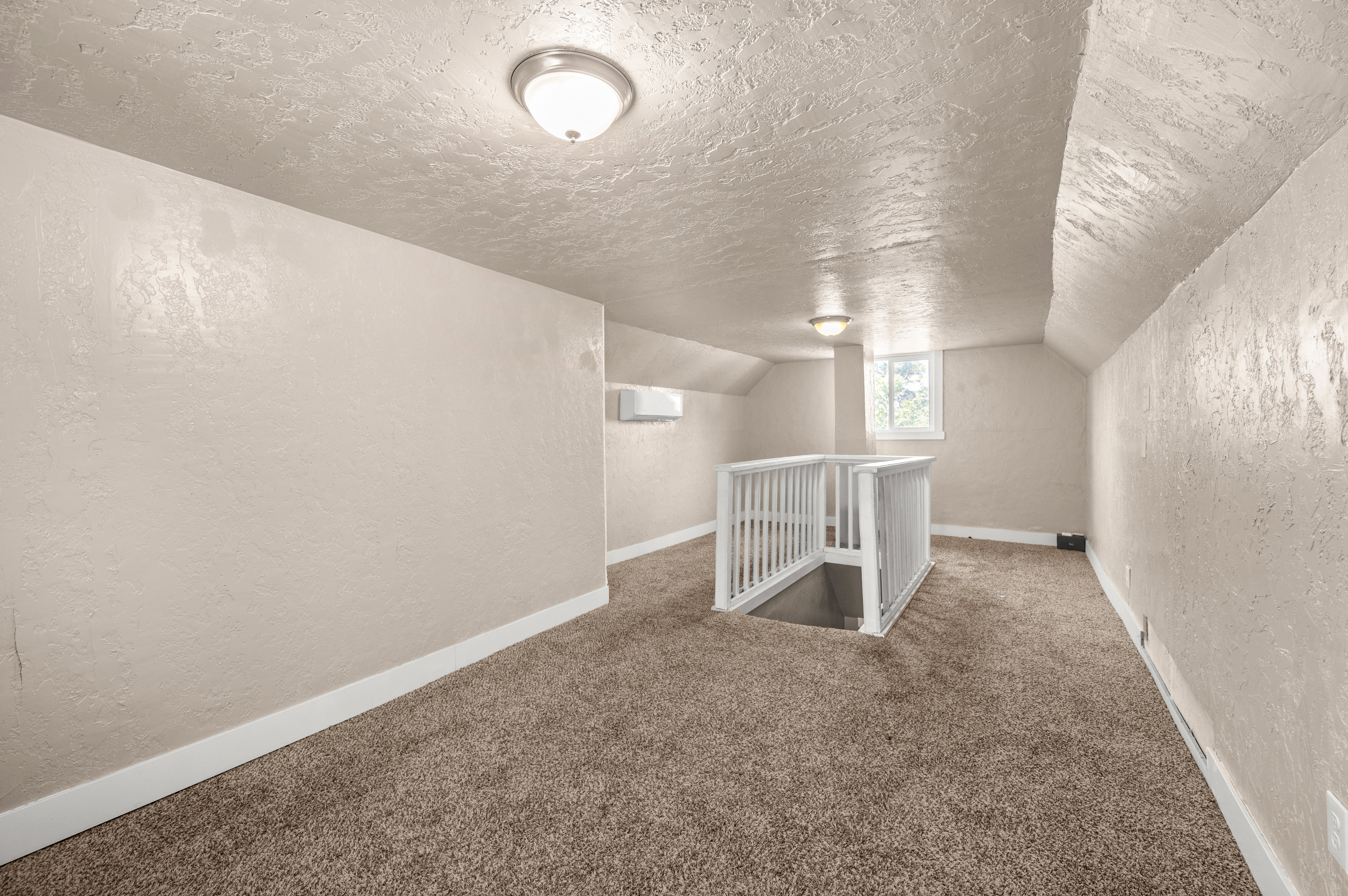Carpeted upper level featuring a white staircase railing, natural light from a window, and two flush-mount ceiling lights