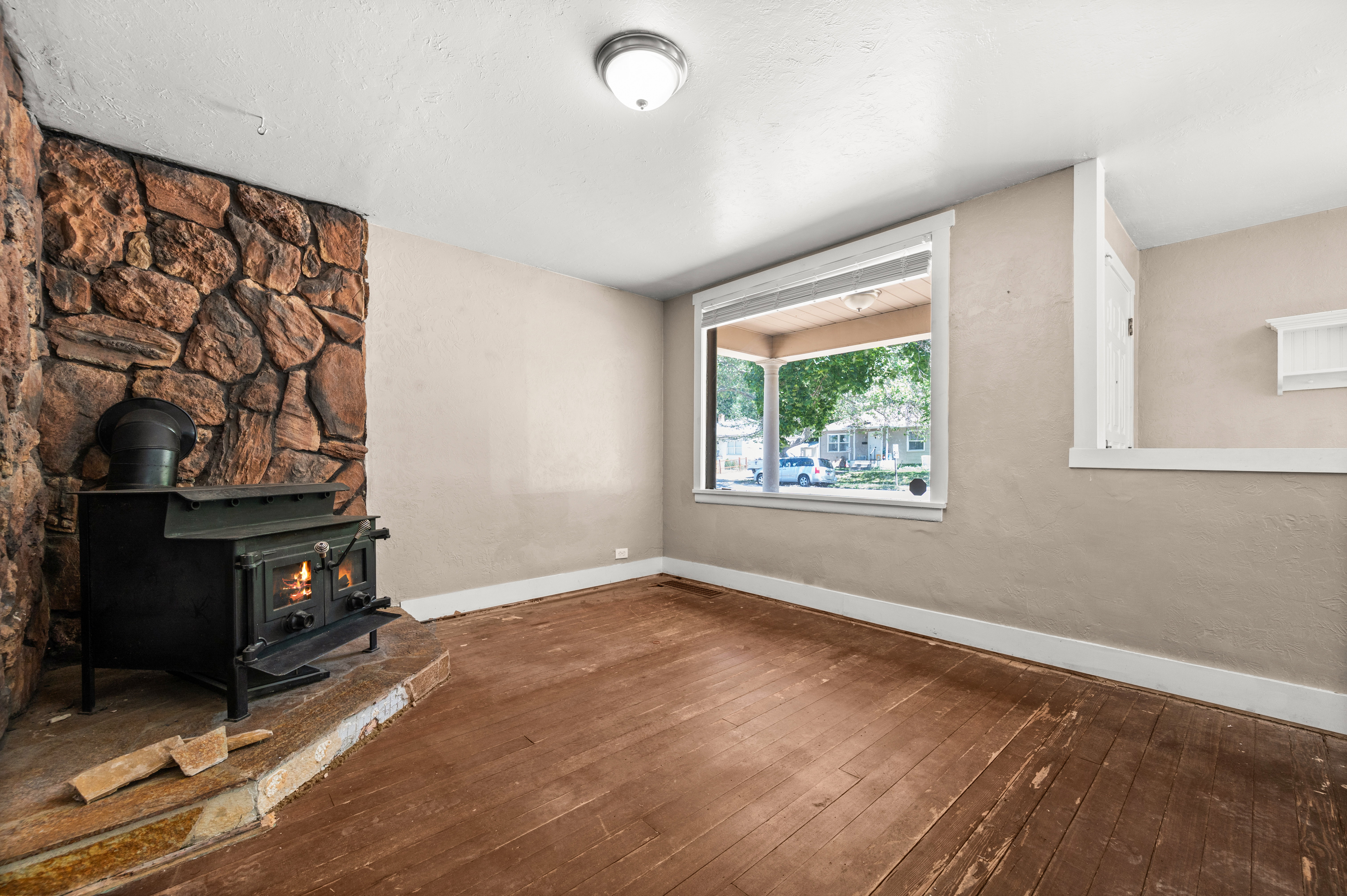 Stone-faced fireplace with a black wood-burning stove, large picture window, and wood-finish flooring