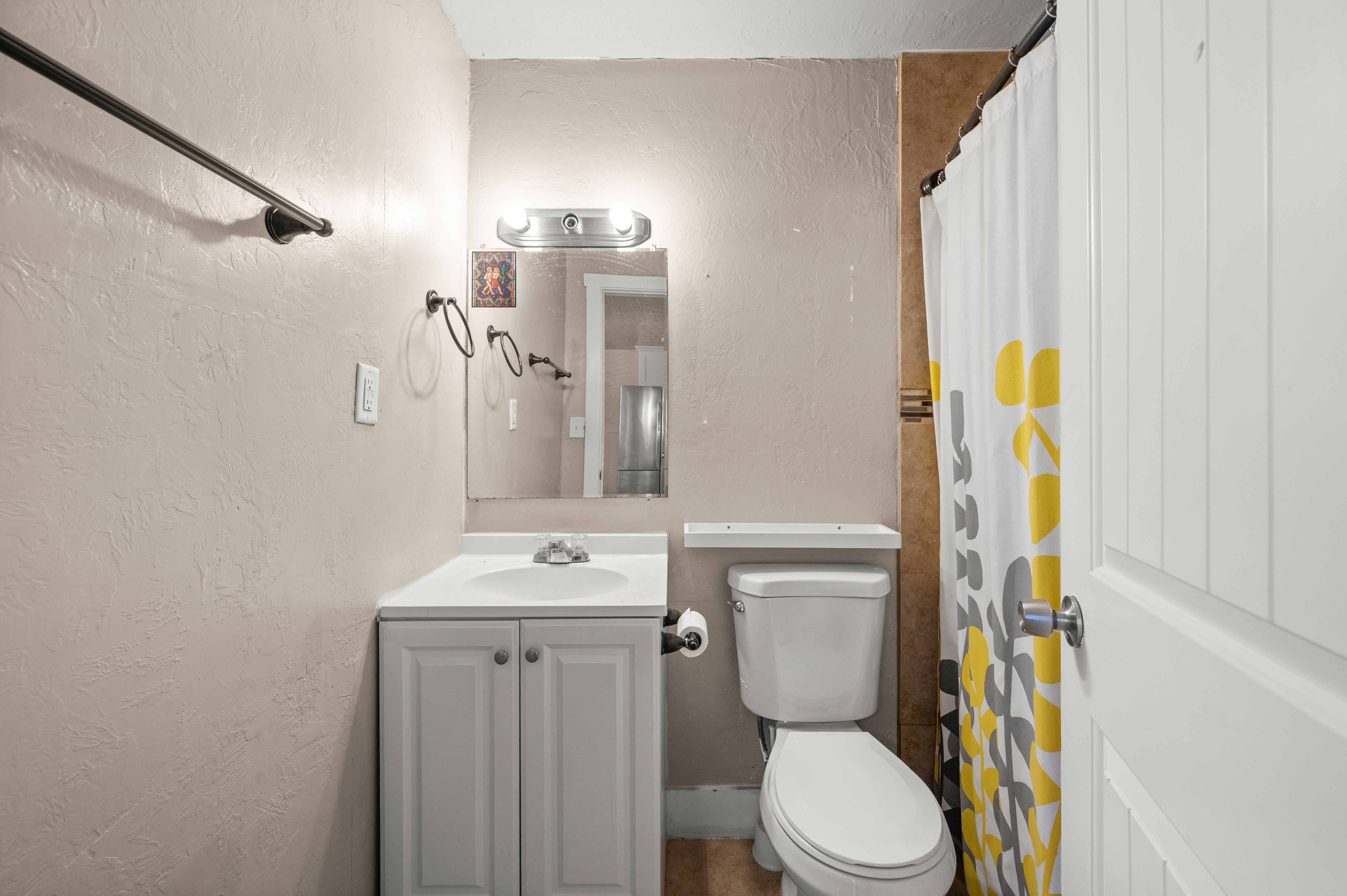 Bathroom featuring a white vanity with integrated sink, a commode, and a shower area with tiled surround
