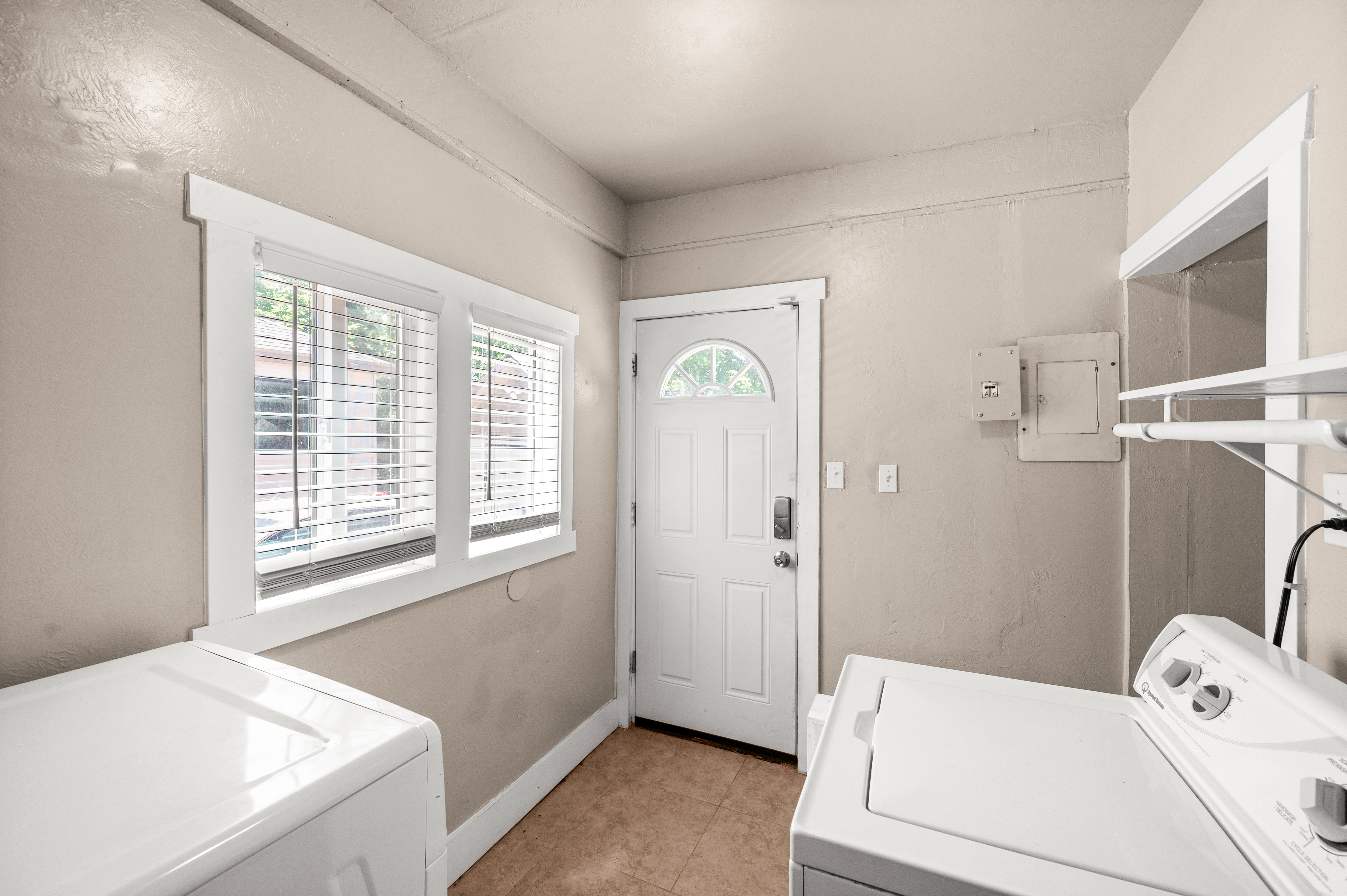 Utility room featuring a window with blinds, a white paneled door with an arched glass insert, and durable tile flooring