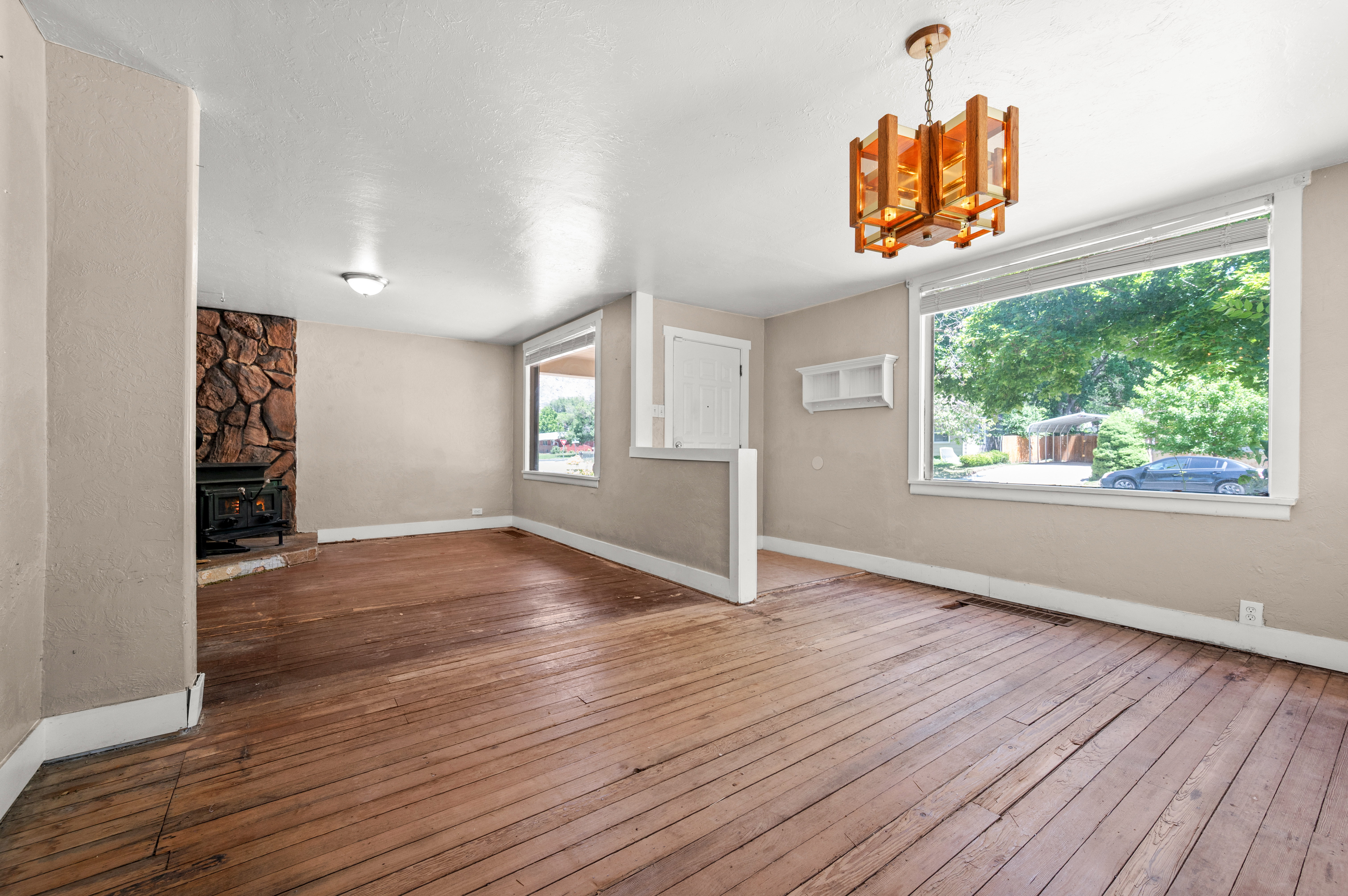 Spacious room featuring exposed wood flooring and a prominent stone-clad fireplace with a wood-burning stove insert