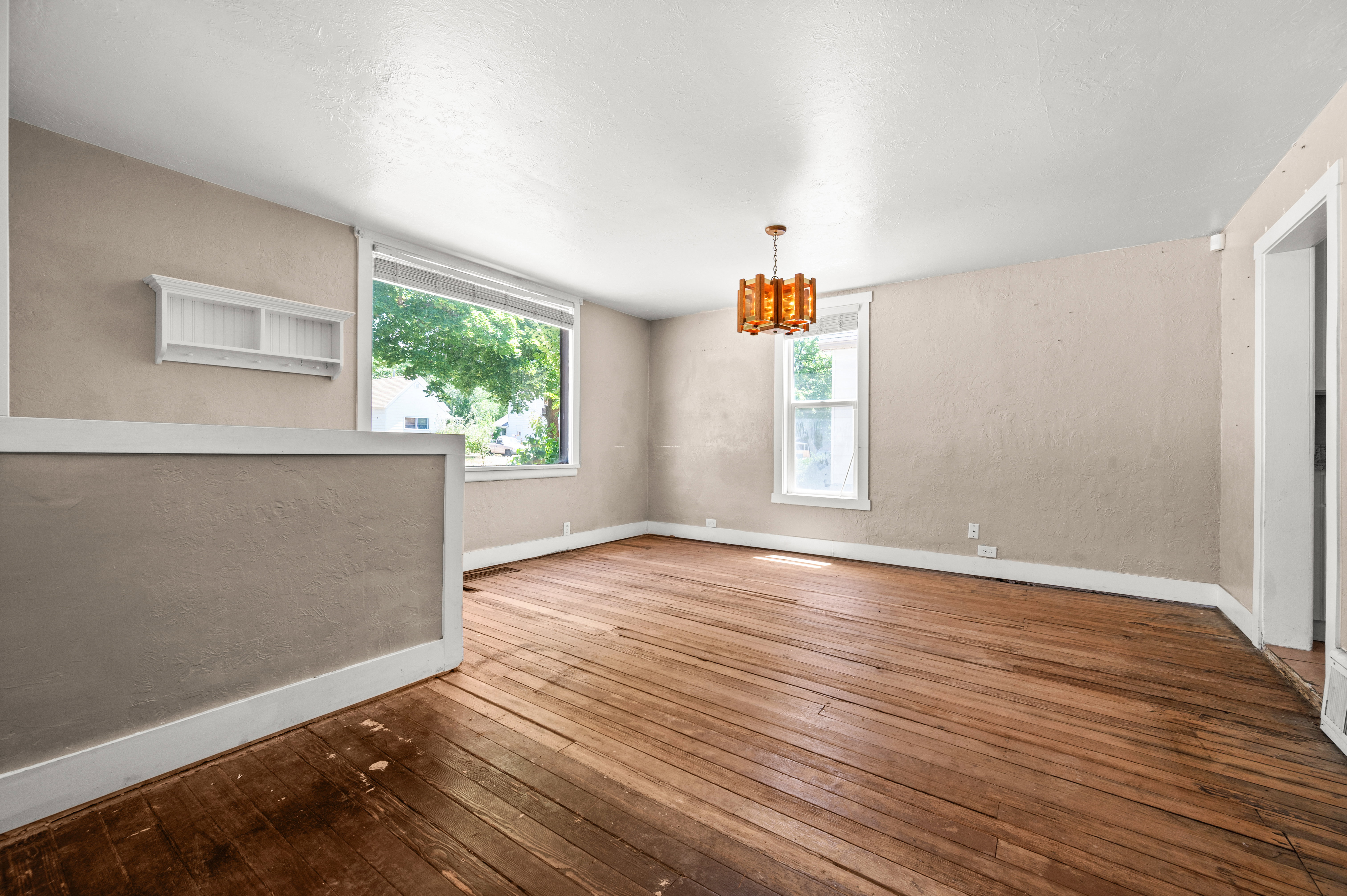 Expansive interior room featuring wide plank wood flooring, a large picture window, a secondary window, and a decorative ceiling light fixture