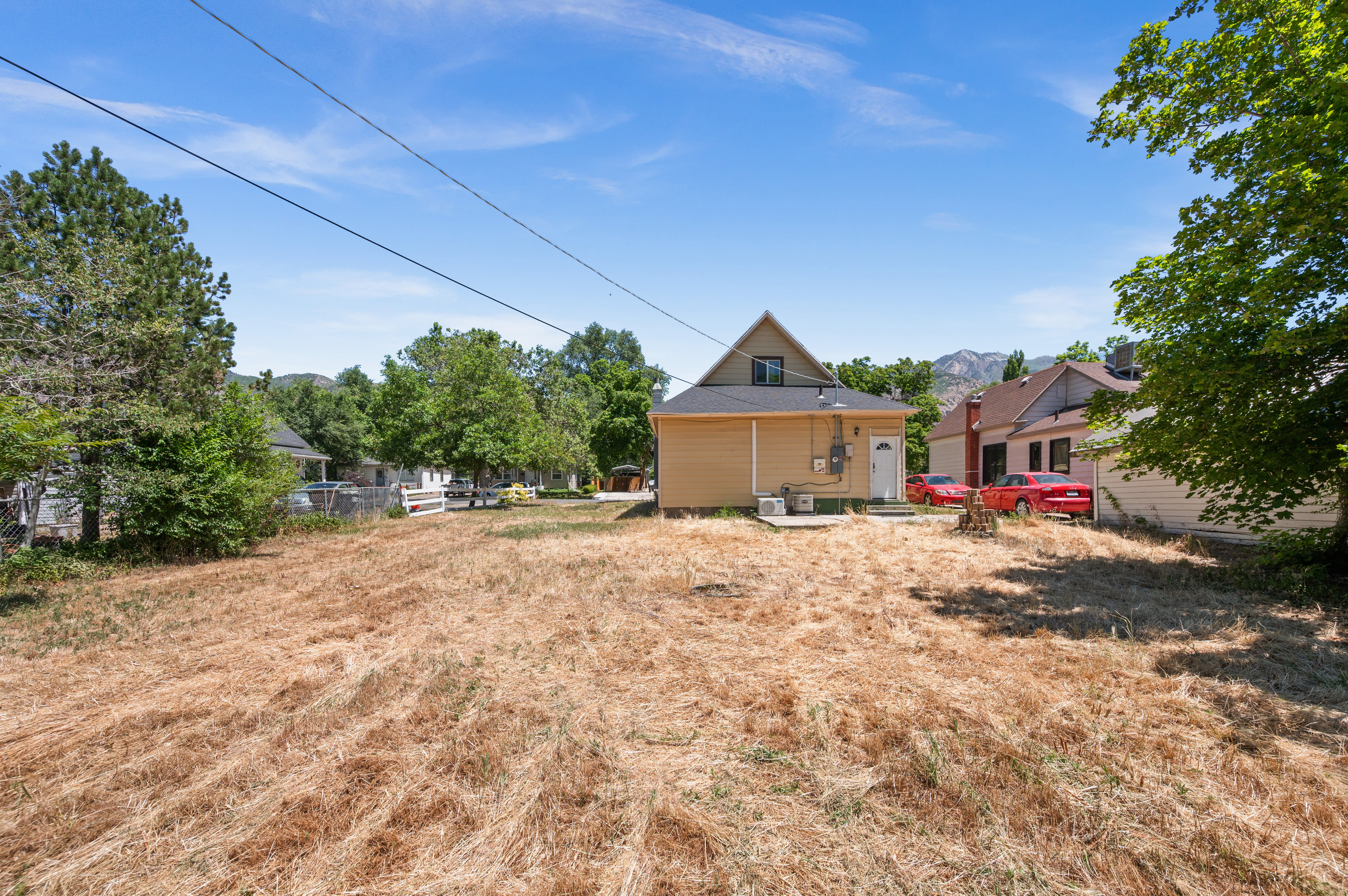 Expansive yard space featuring a yellow-sided home with a dormer window, an additional single-story structure, mature trees, and mountain scenery in the background