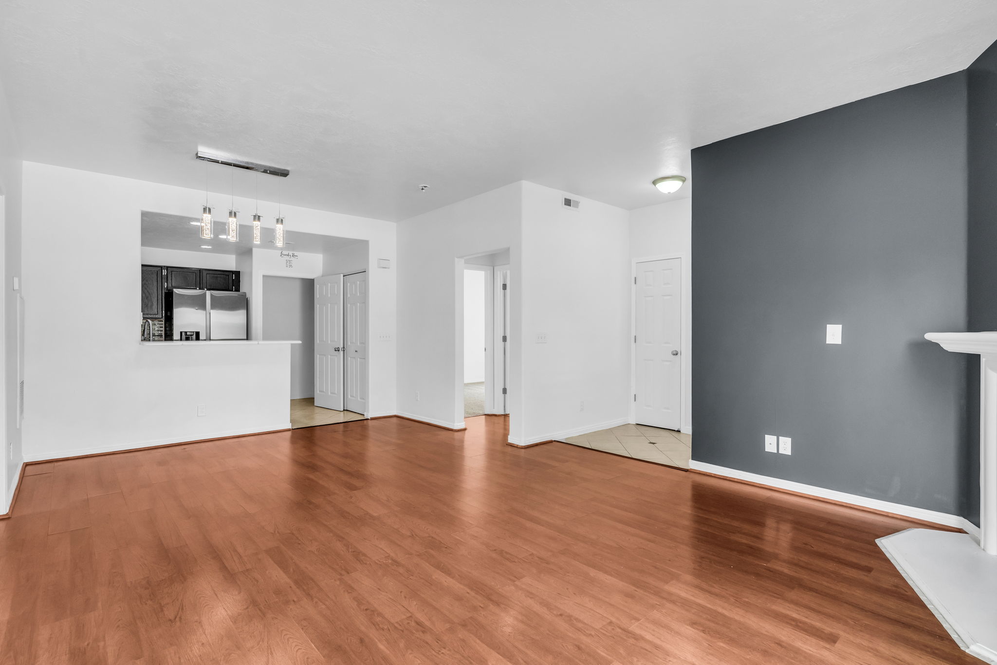 Open concept living area featuring wood-finish flooring, a neutral color palette, and a kitchen pass-through with pendant lighting