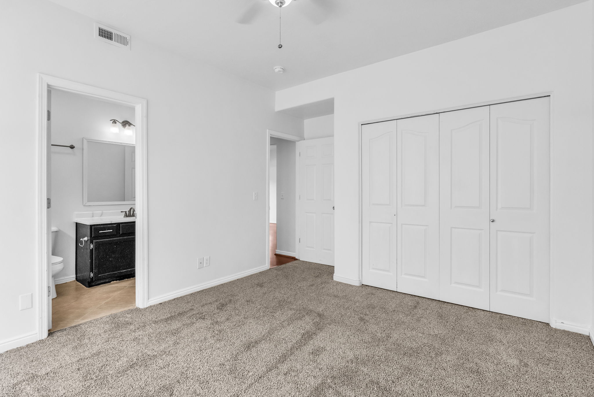 Spacious room featuring neutral carpeting, white walls, and a ceiling fan with integrated lighting