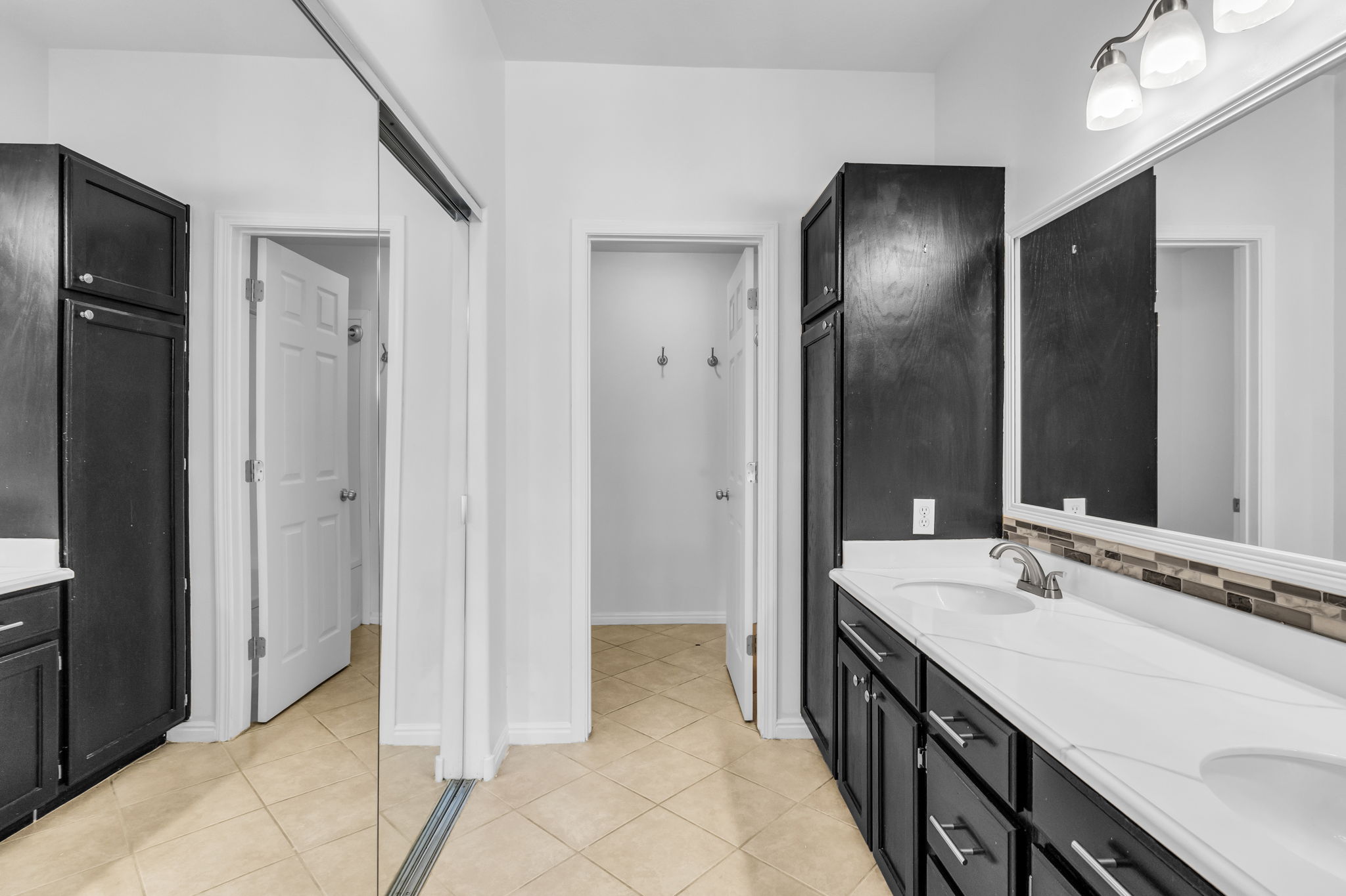 Spacious bathroom featuring dual vanities with white countertops, dark wood-finish cabinetry, and a full-width mirror