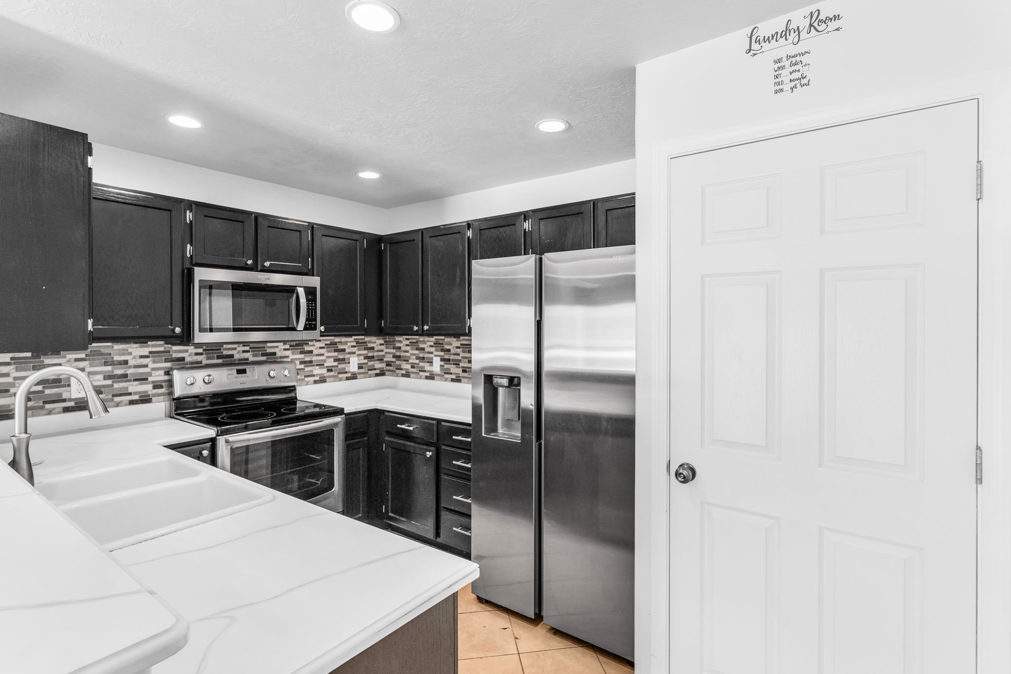 Kitchen featuring dark wood cabinetry, white countertops, stainless steel appliances, a mosaic tile backsplash, and recessed lighting