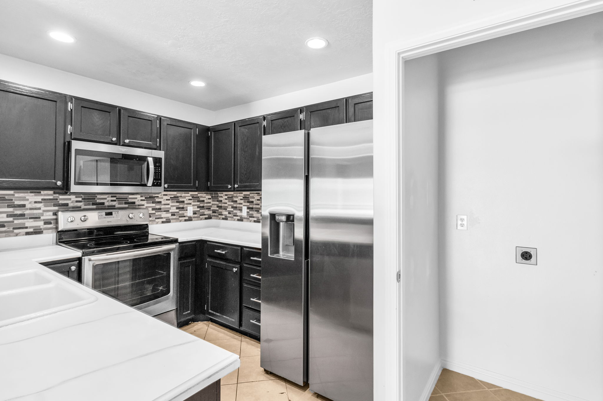 Kitchen featuring dark wood cabinetry, stainless steel appliances, a mosaic tile backsplash, and light-toned countertops