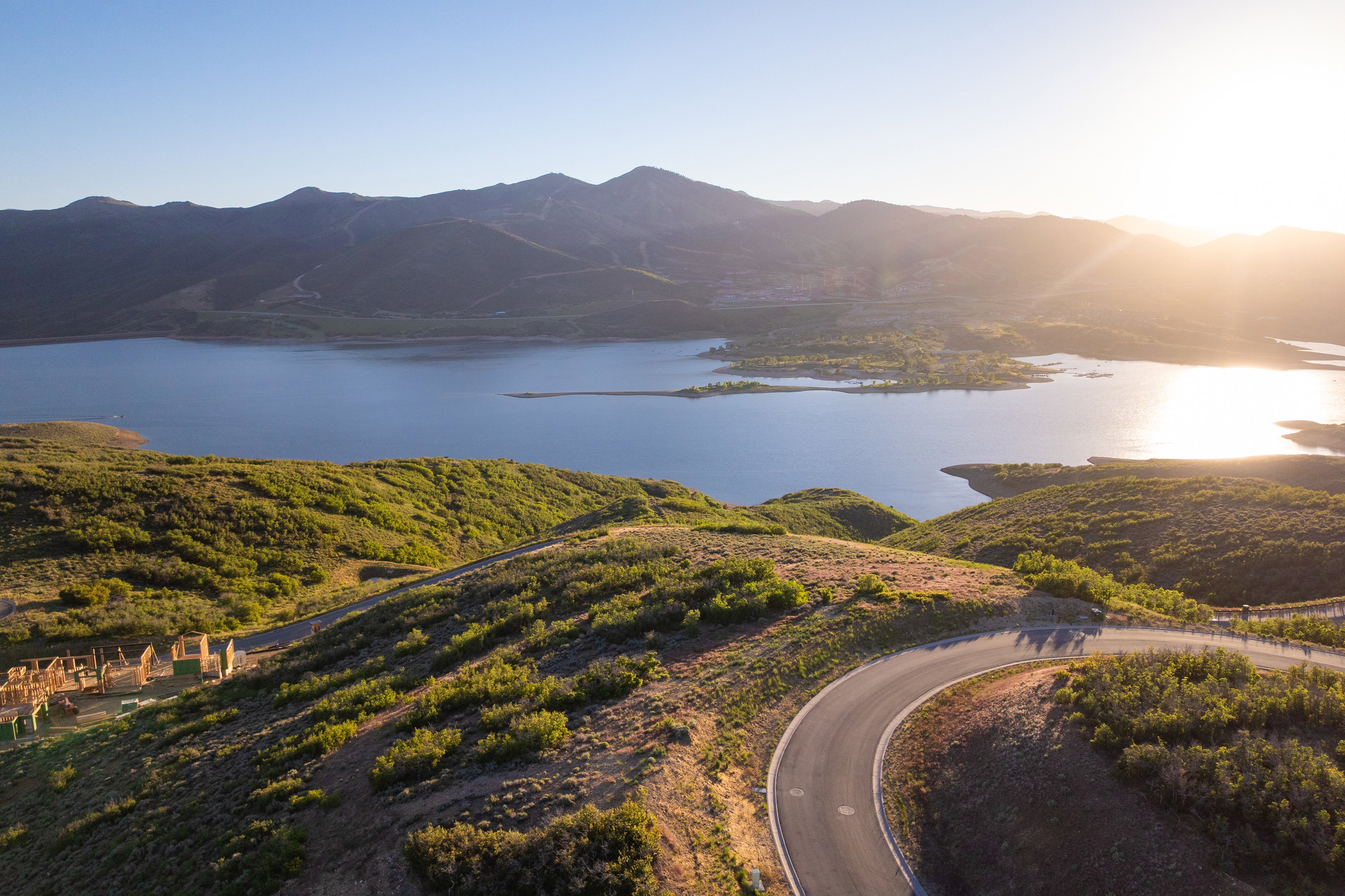 Winding paved road ascending a verdant hillside, offering expansive water frontage and mountain terrain