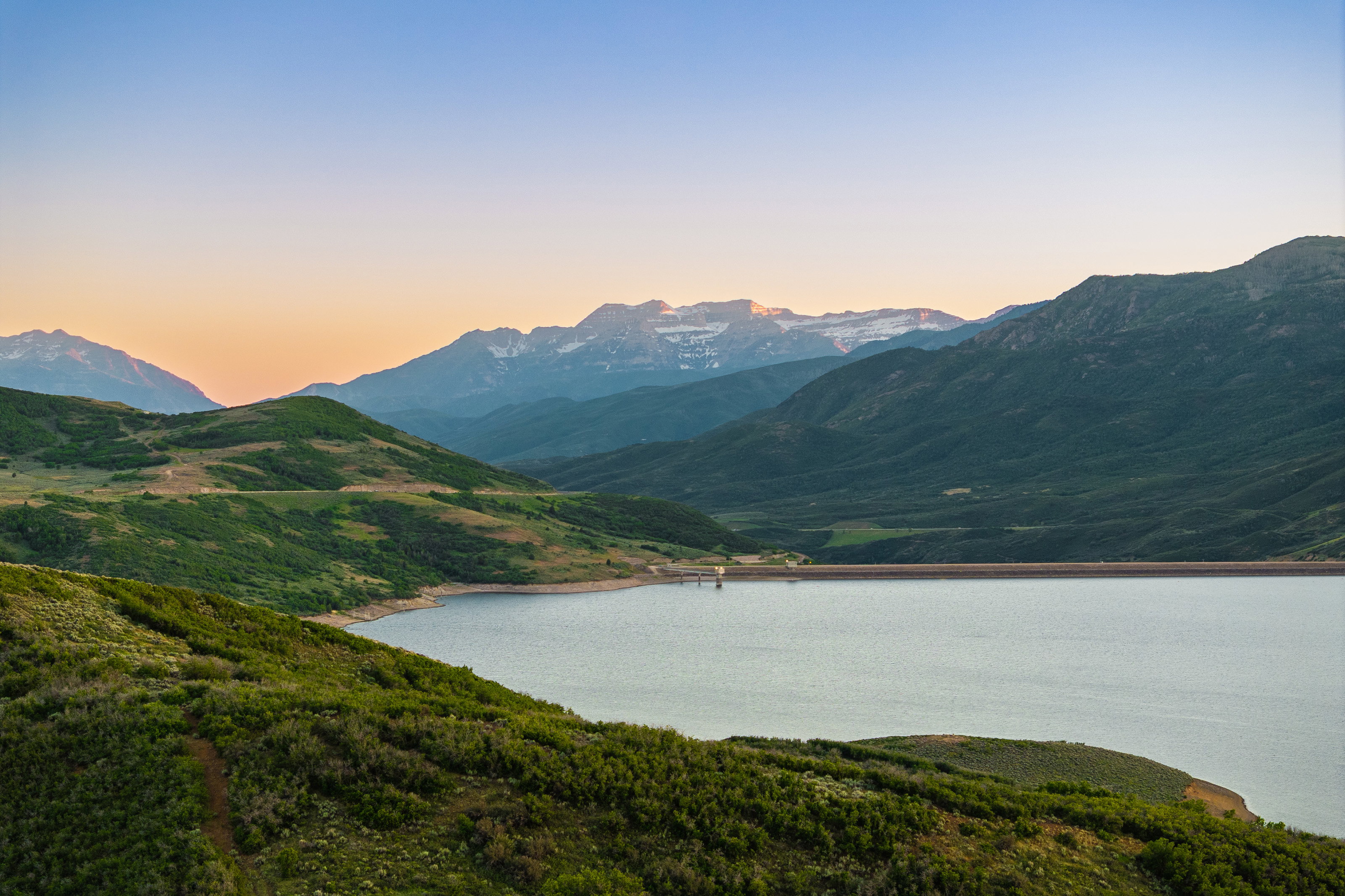 Expansive reservoir bordered by verdant hillsides and distant snow-capped mountains