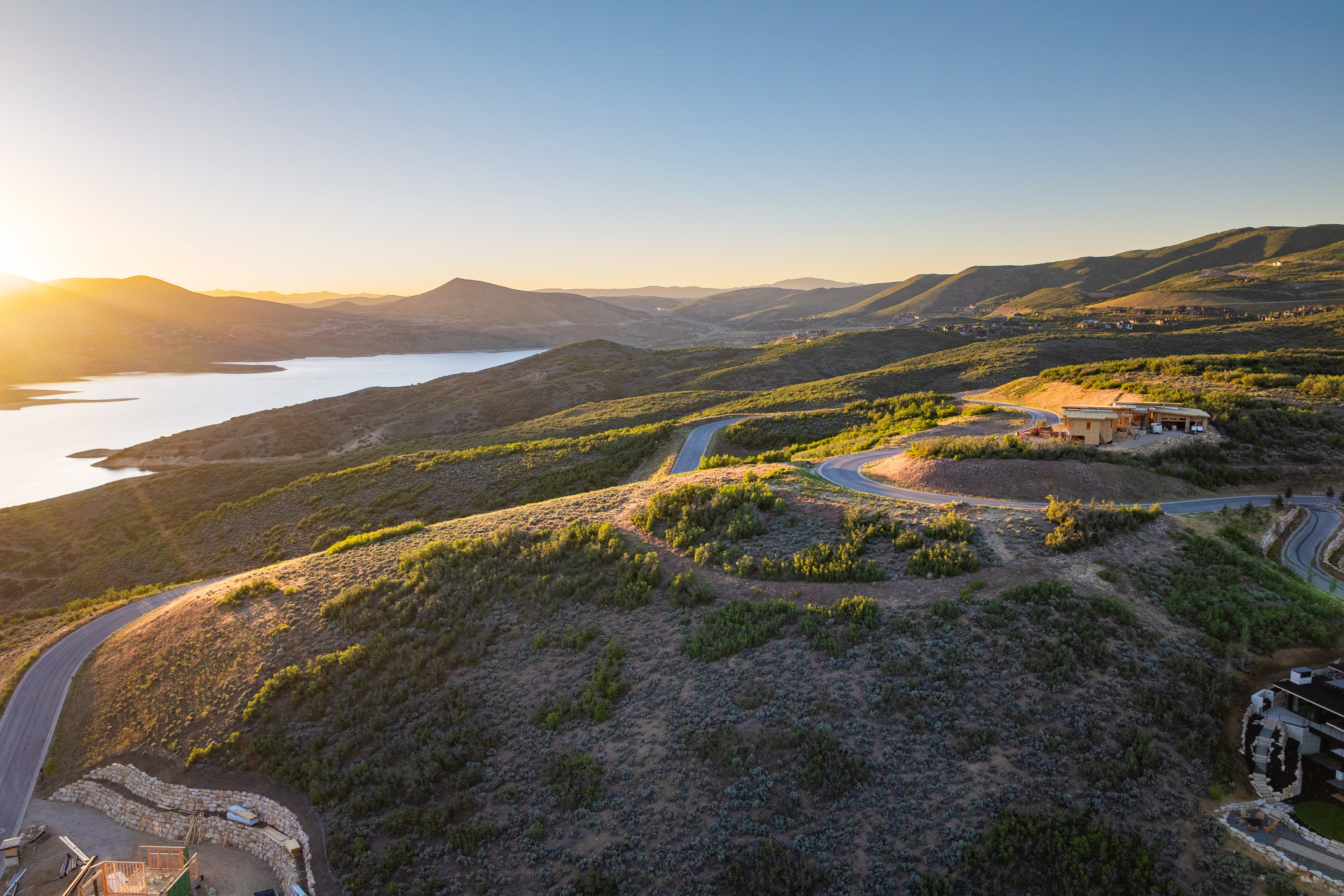 Expansive mountain landscape featuring a large body of water, meandering roads, and distant residential structures