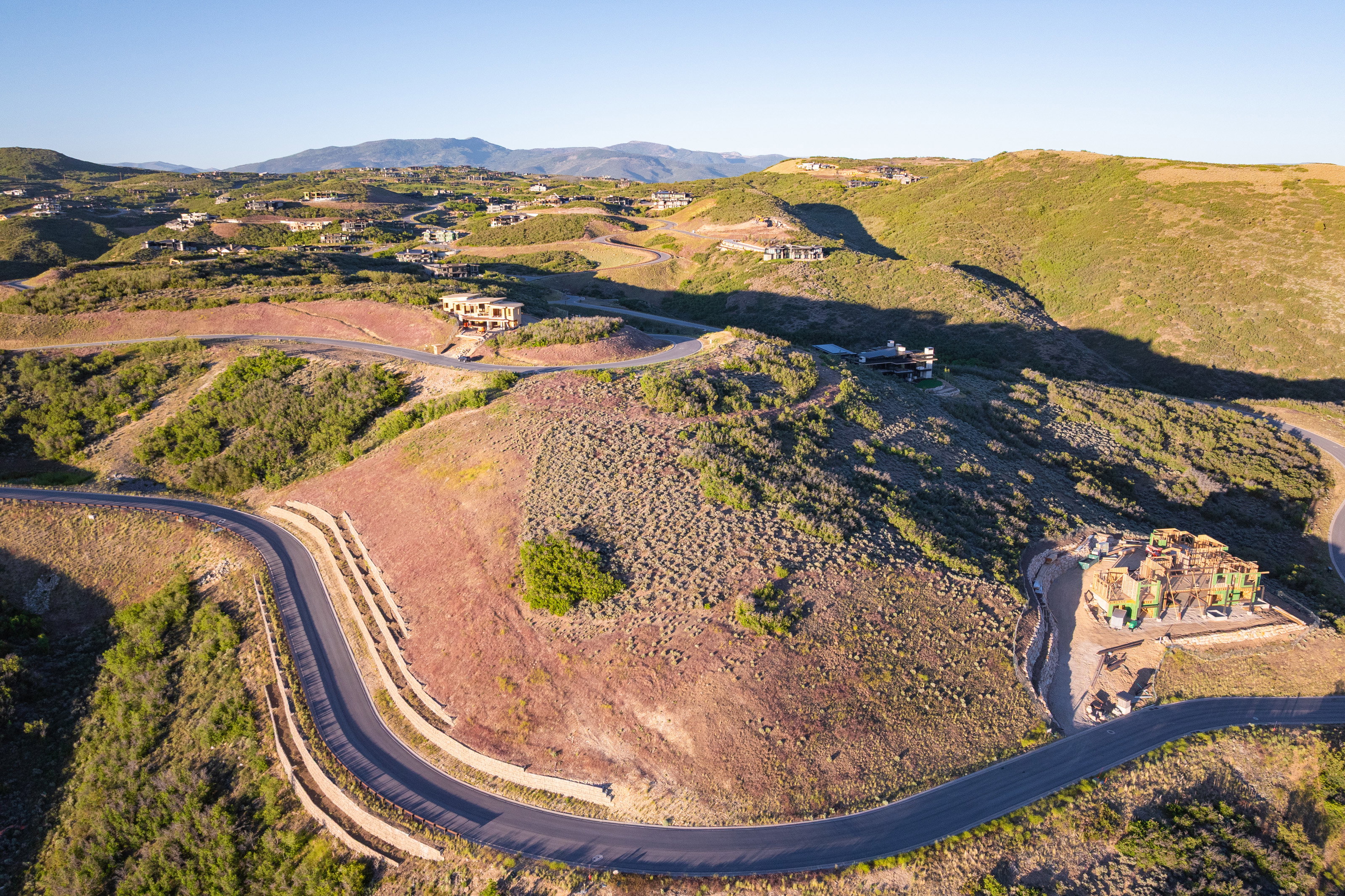 Curving paved road traversing a terraced hillside with established brush and distant mountainous terrain