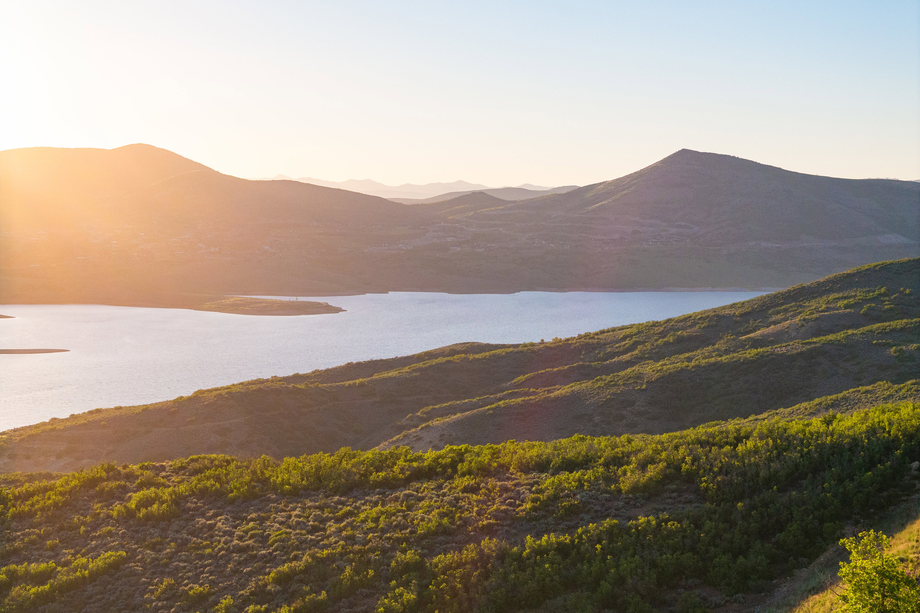 Expansive mountain landscape featuring a large body of water, rolling hills covered in natural vegetation, and distant mountain ranges