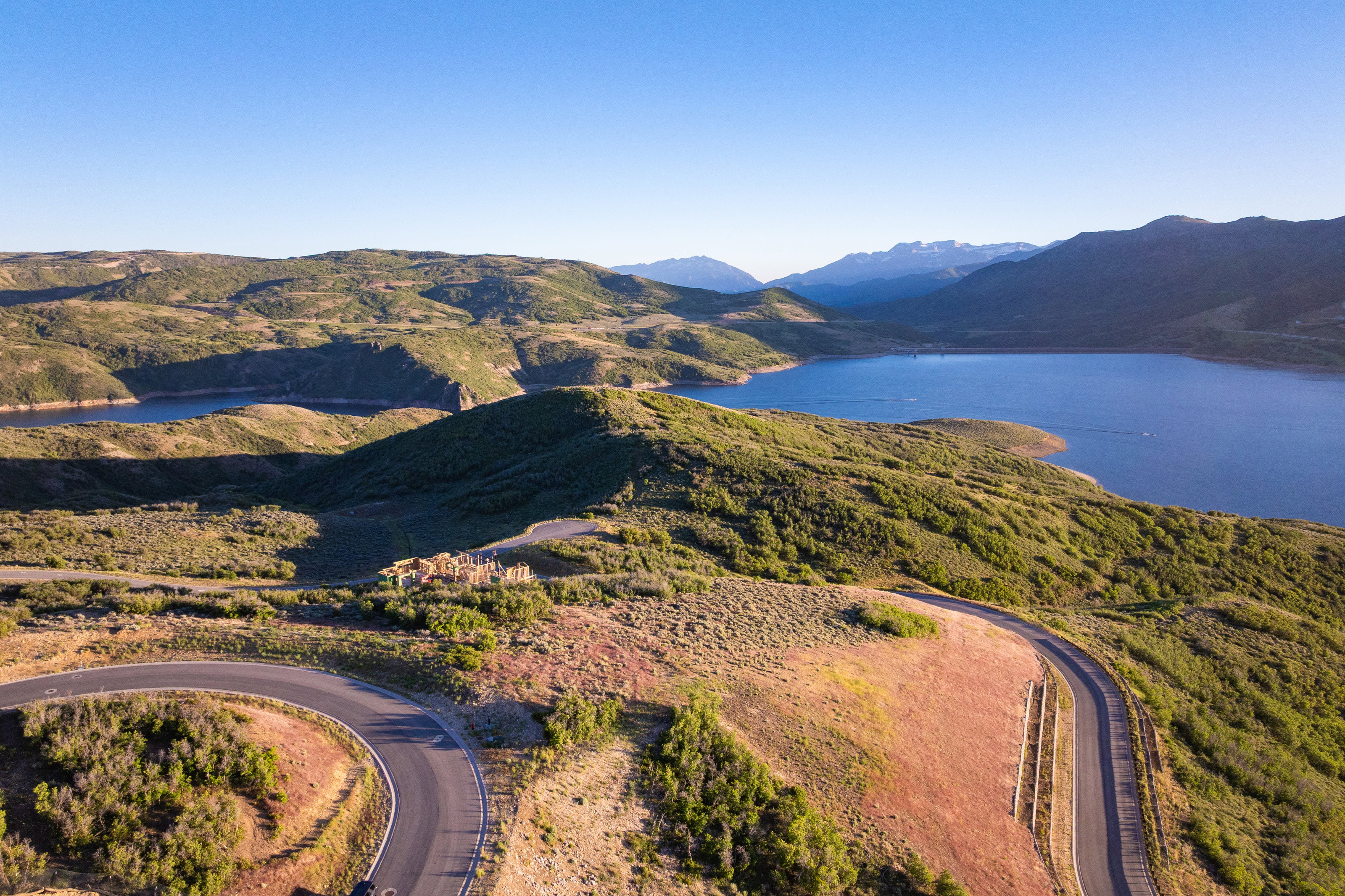 Expansive natural landscape featuring a large body of water, distant mountains, and winding paved roads