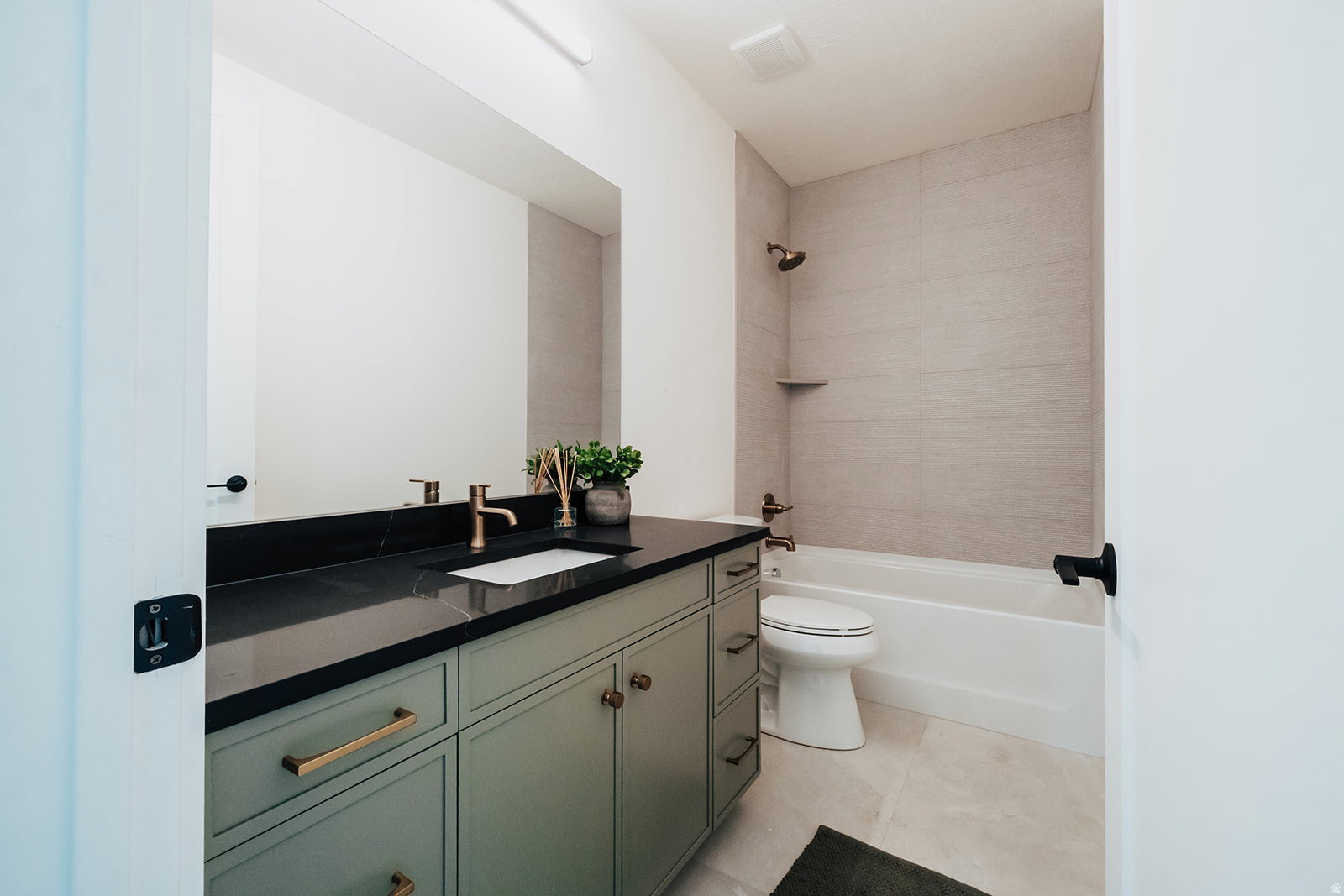 Bathroom featuring a sage green vanity with brass hardware, a dark countertop, an undermount sink, and a large wall mirror