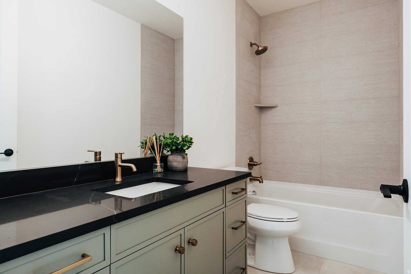 Bathroom featuring a light green vanity with brass hardware, a dark countertop with an integrated rectangular sink, and a large wall mirror