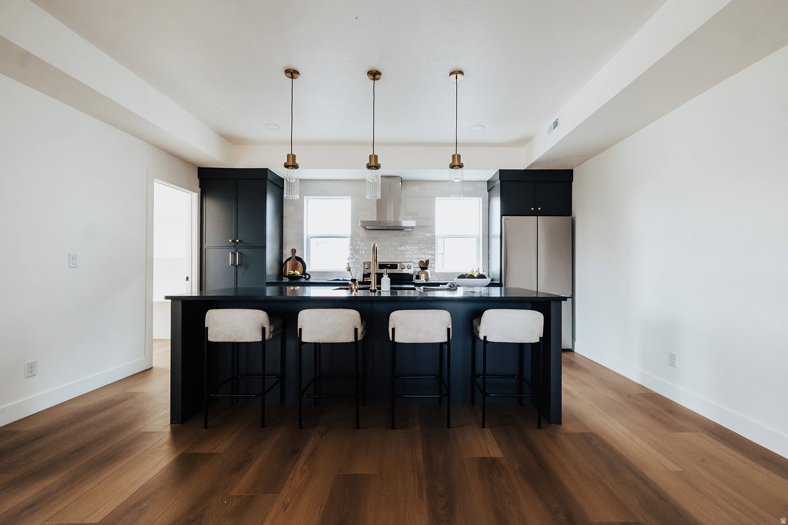Spacious kitchen featuring dark cabinetry, stainless steel appliances, a center island with seating, a tile backsplash, and wood-finish flooring