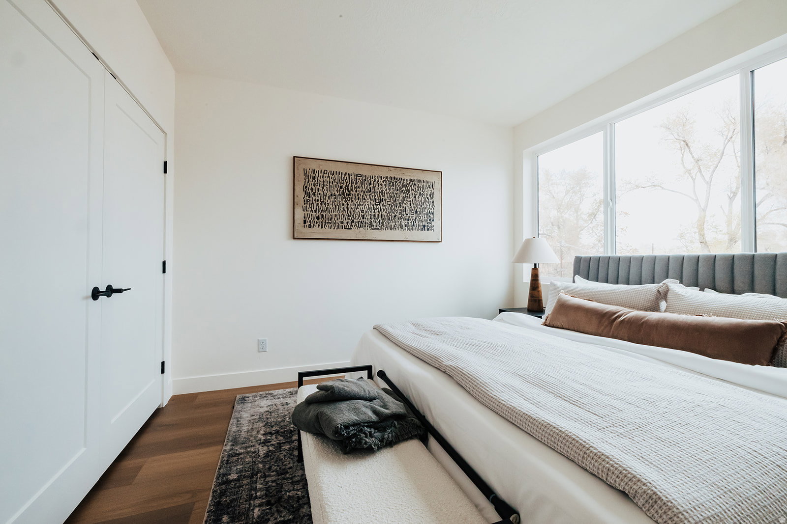 Bright bedroom featuring wide plank wood-finish flooring, white trim, and a full wall of windows