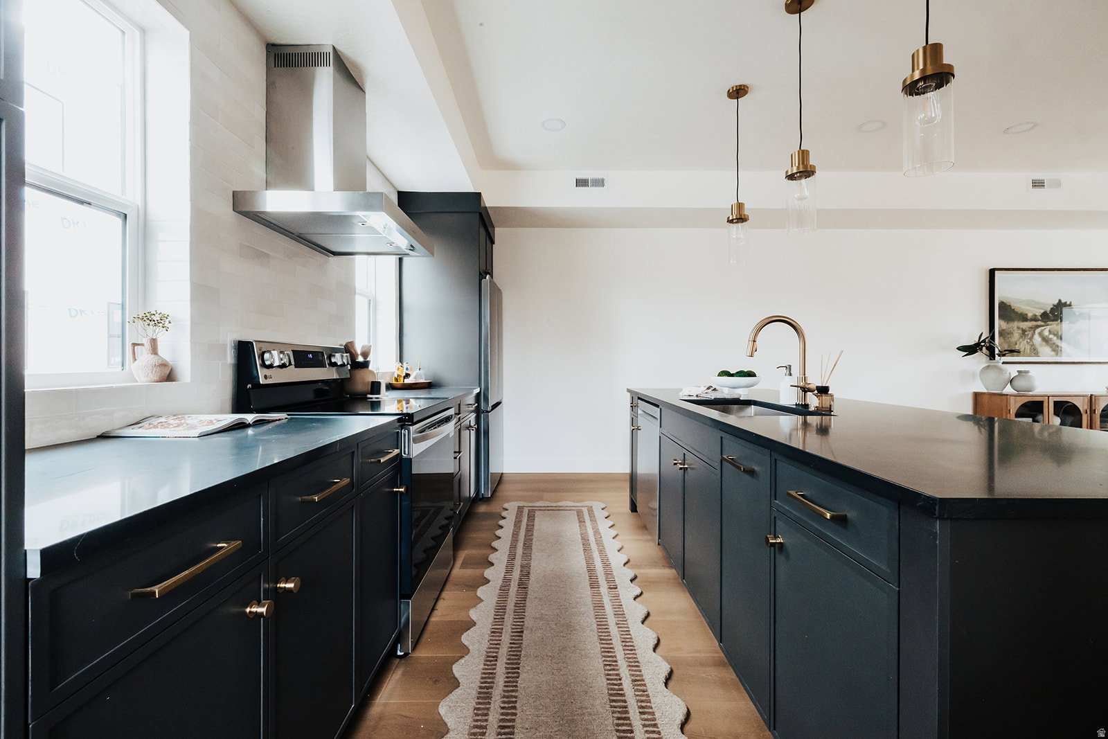 Kitchen featuring a large central island, dark cabinetry with brass hardware, light wood-finish flooring, stainless steel appliances, and pendant lighting