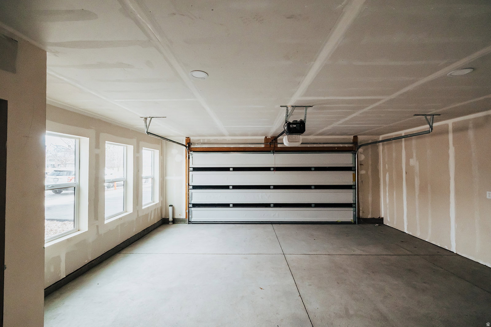 Spacious garage featuring a concrete floor, three windows providing natural light, a modern sectional garage door, and an automatic garage door opener