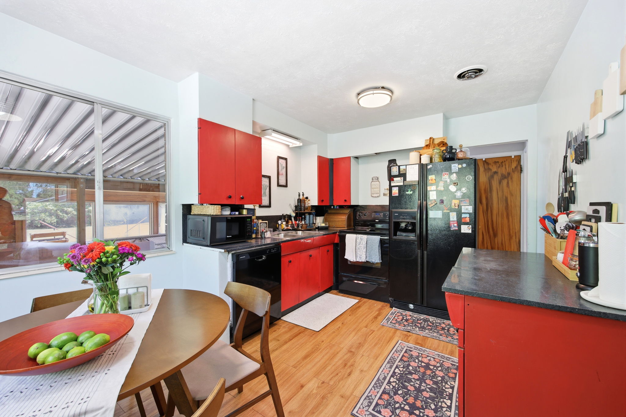 Kitchen featuring bold red cabinetry, black appliances, and wood-finish flooring
