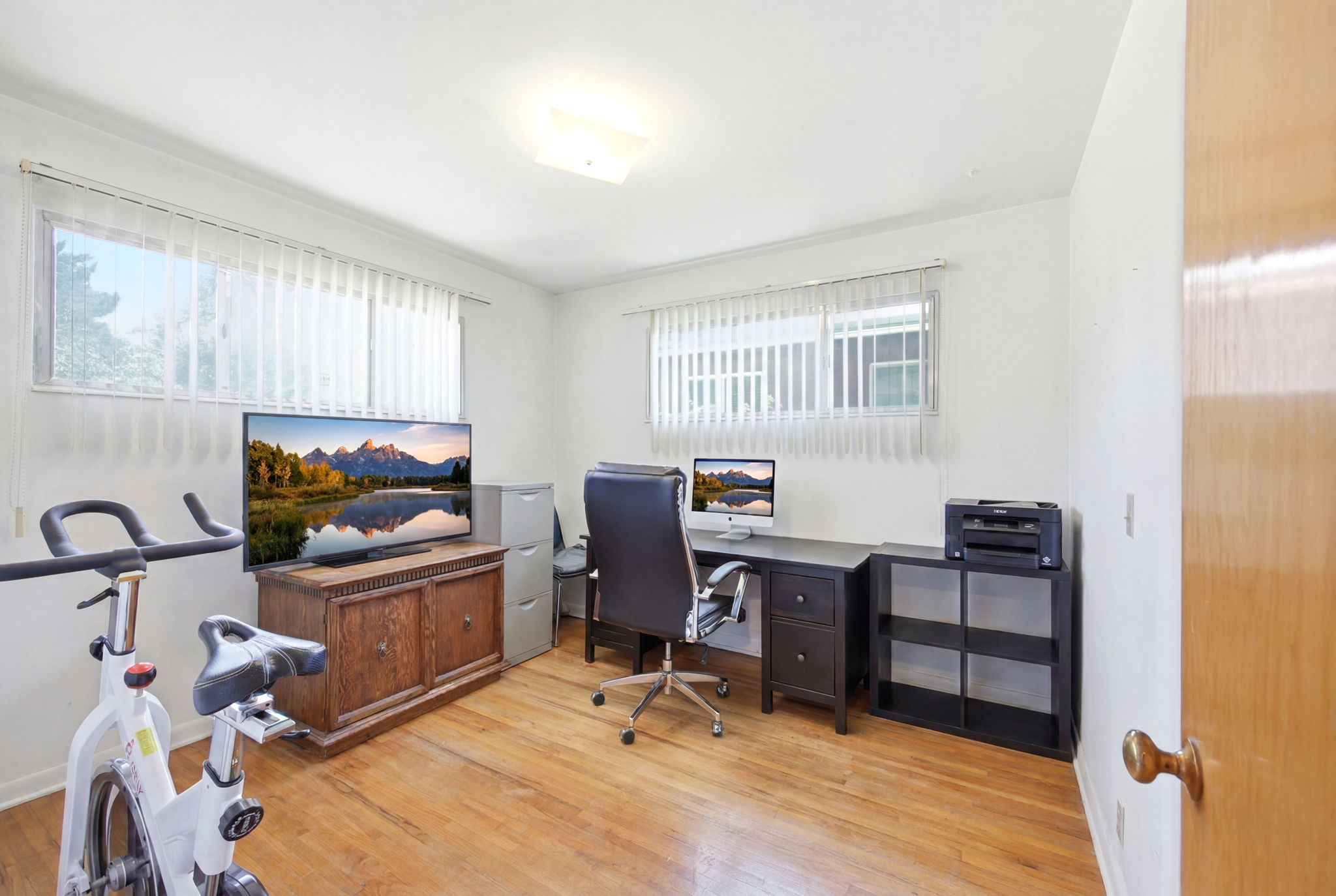 Room featuring wood-finish flooring, two large windows with blinds, and white painted walls