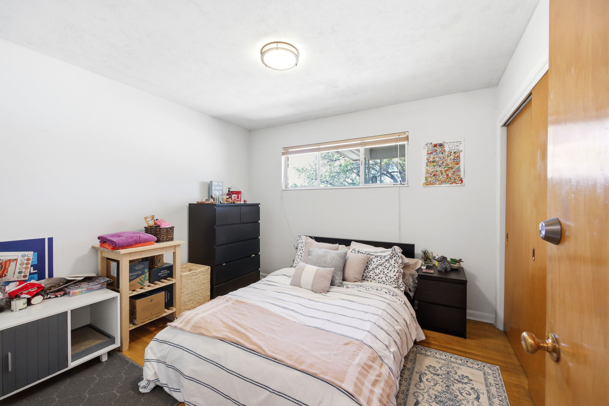 Bedroom featuring wood-finish flooring, a window with natural light, a ceiling-mounted light fixture, and a built-in closet with a wood-panel door