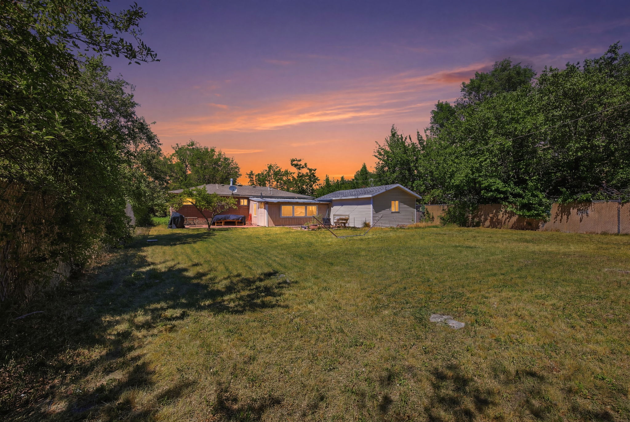 Expansive rear yard featuring a grass lawn, mature perimeter trees, and a detached auxiliary structure