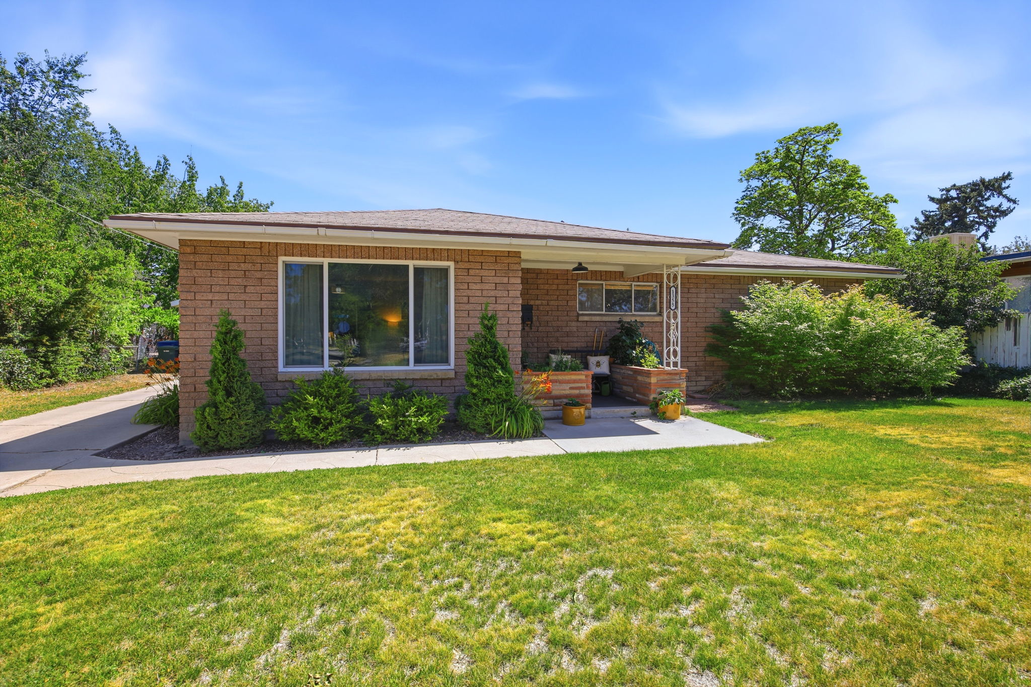 Brick exterior featuring a front porch with white columns, a large picture window, a paved driveway, and mature landscaping