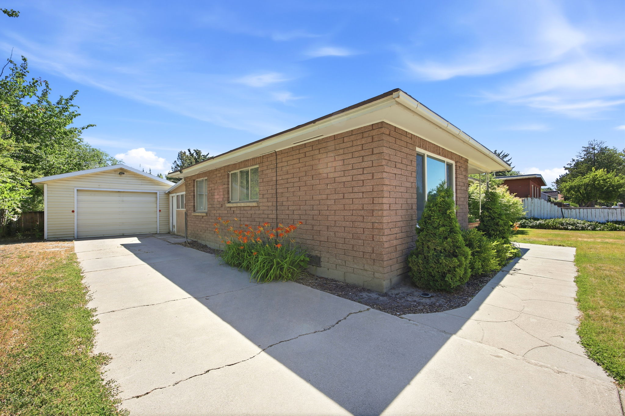 Brick exterior featuring a single-story design, an attached garage, a concrete driveway, a concrete walkway, and established landscaping