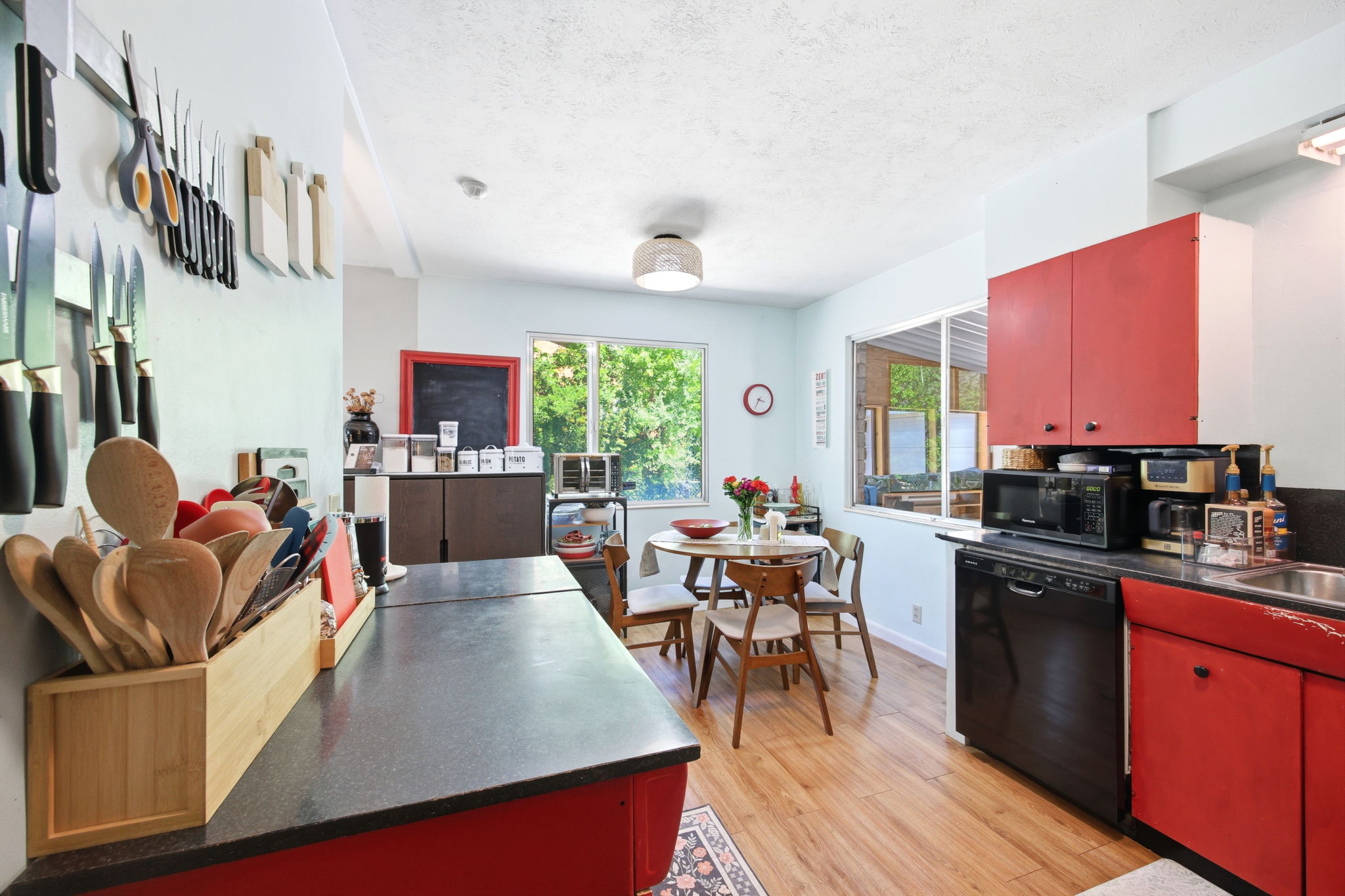 Kitchen featuring red cabinetry, wood-finish flooring, a black countertop, and a built-in black dishwasher