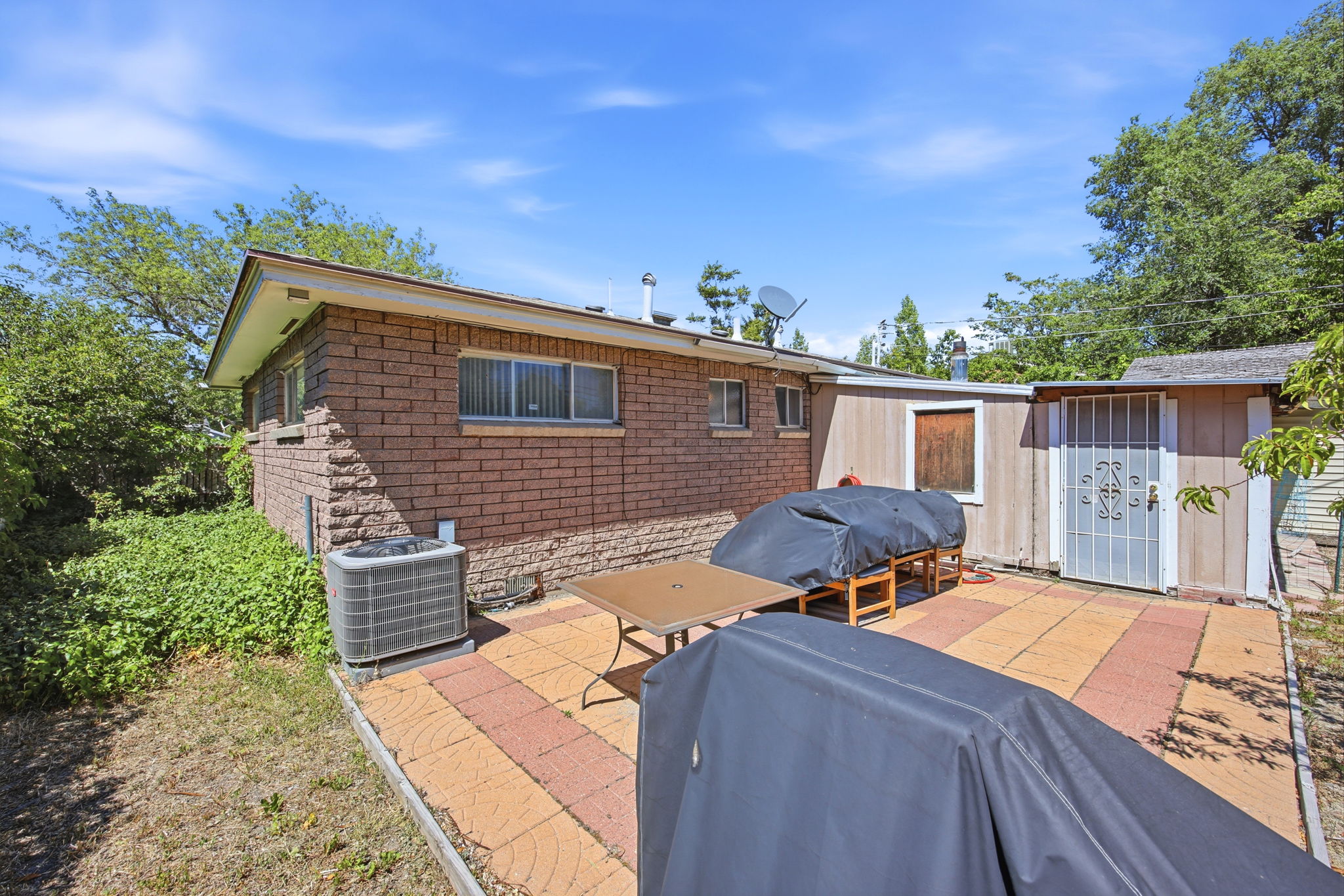 Rear exterior featuring brick siding, multi-colored paver patio, and an outbuilding with a security door