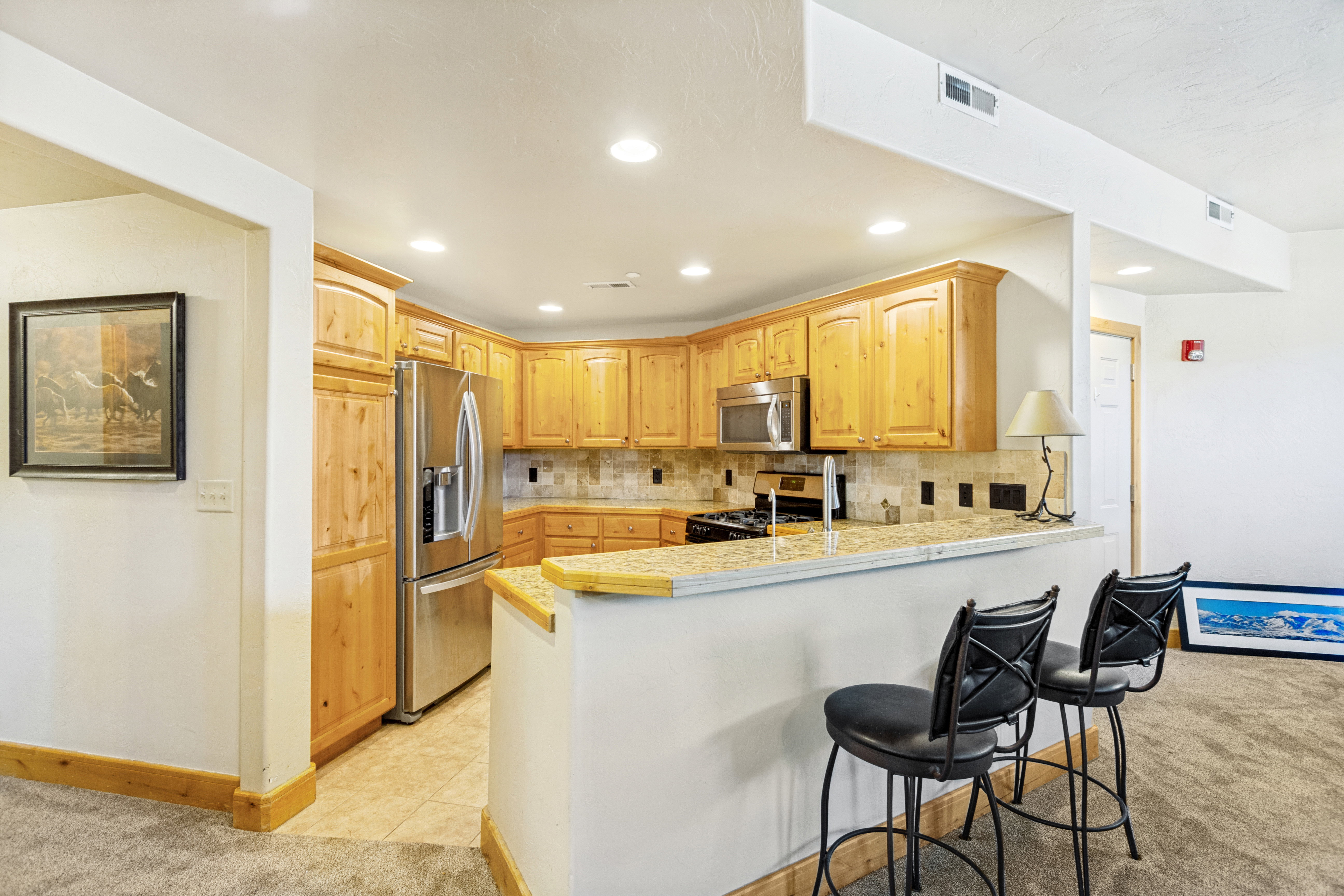 Kitchen featuring light wood cabinetry, stainless steel appliances, a stone-finish countertop, and a tiled backsplash