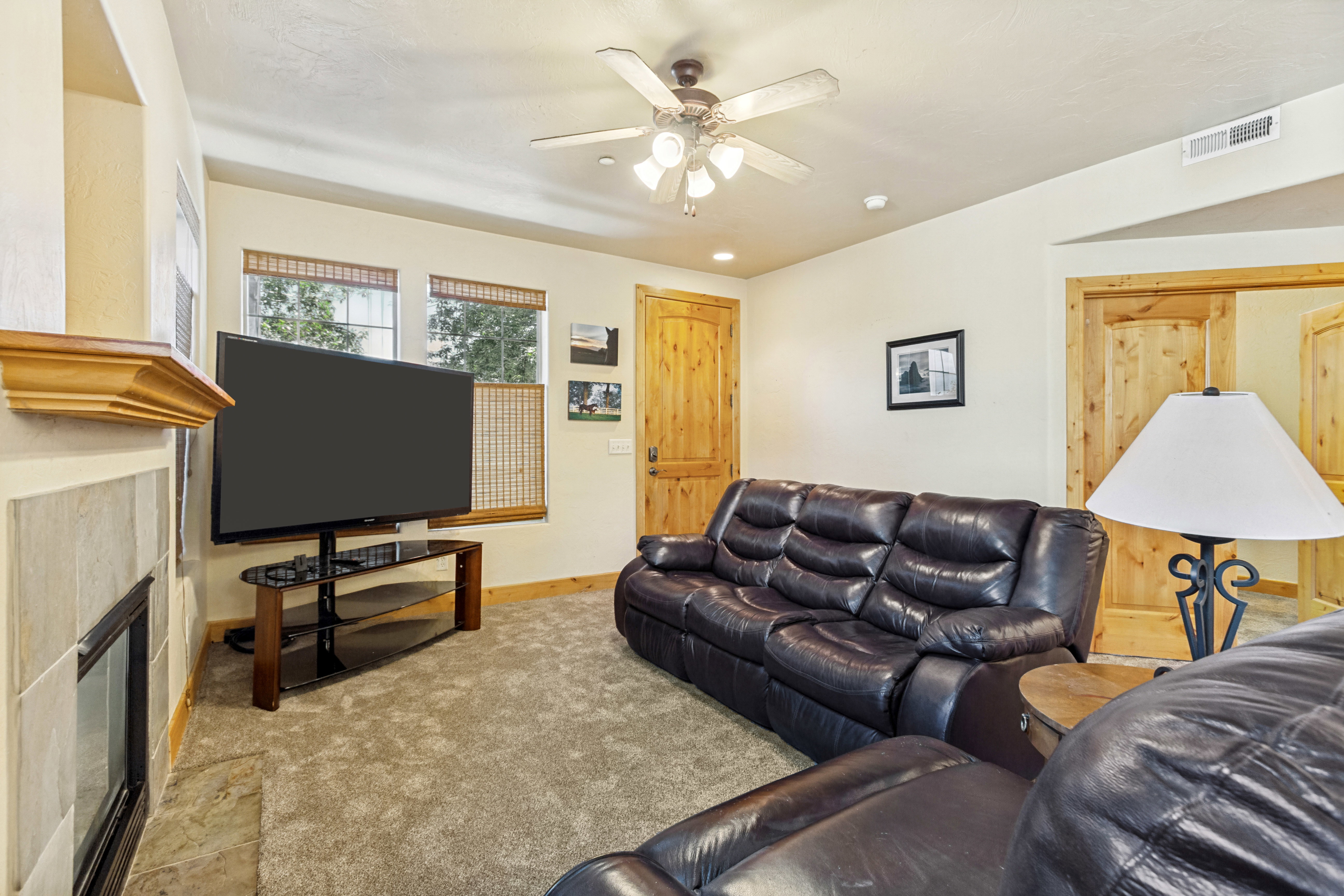 Living area featuring a floor-to-ceiling tiled fireplace, two windows with natural wood blinds, a ceiling fan with integrated lighting, and knotty pine doors