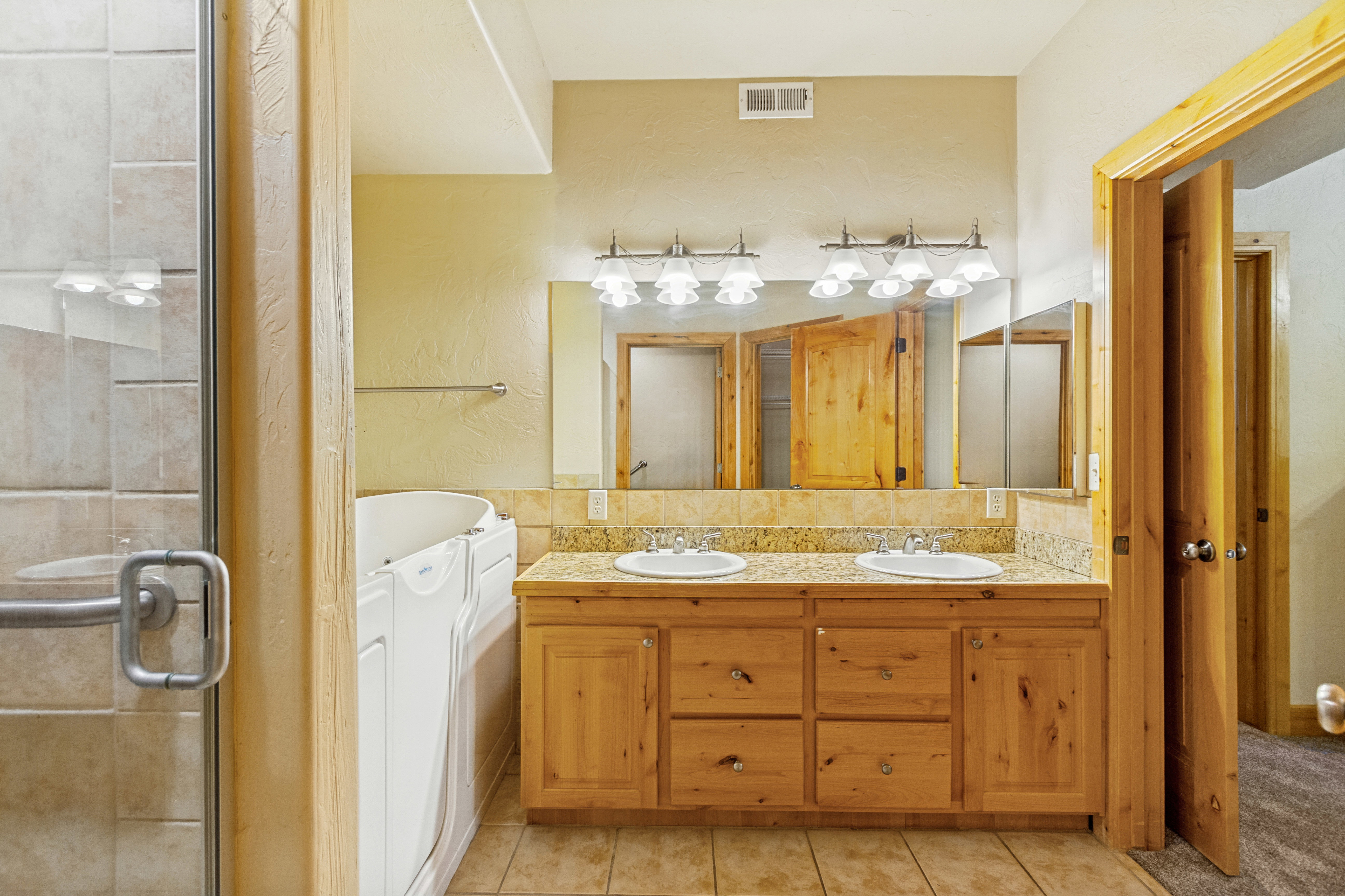 Bathroom featuring a double vanity with light wood cabinetry, dual undermount sinks, and a stone-look countertop