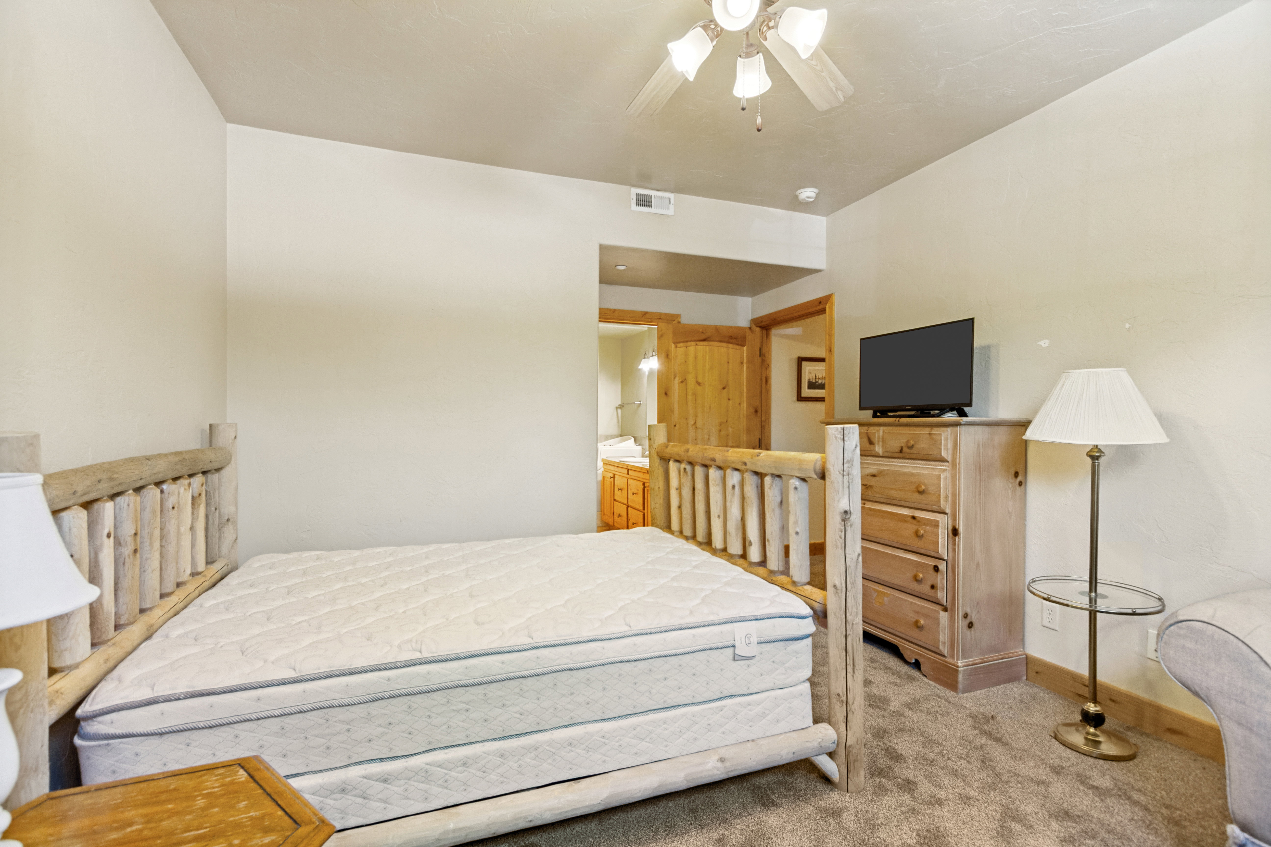 Carpeted room featuring a ceiling fan, light-toned walls, and a wood-finish bed frame