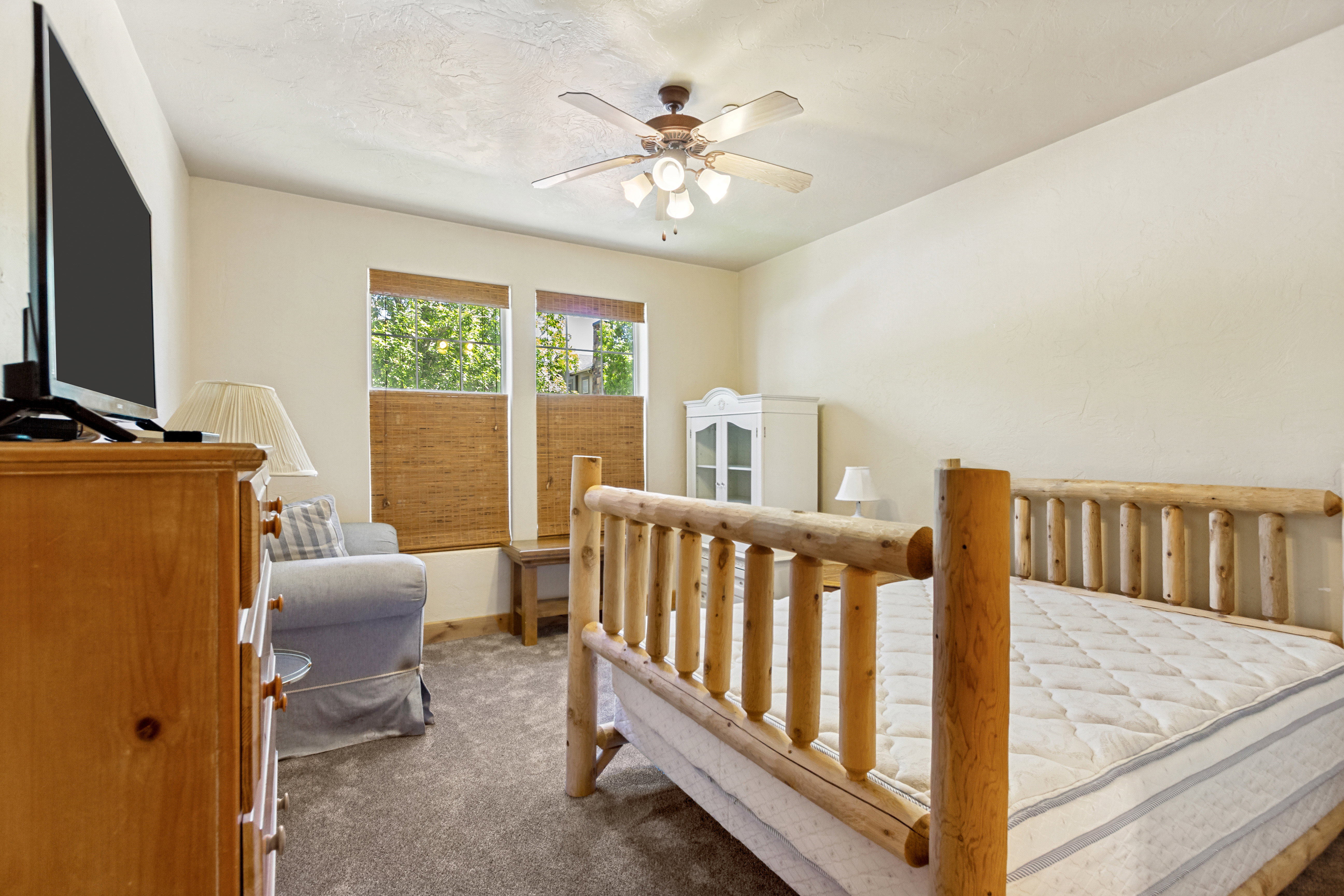 Carpeted room with a ceiling fan, two windows with woven shades, and a light wood dresser