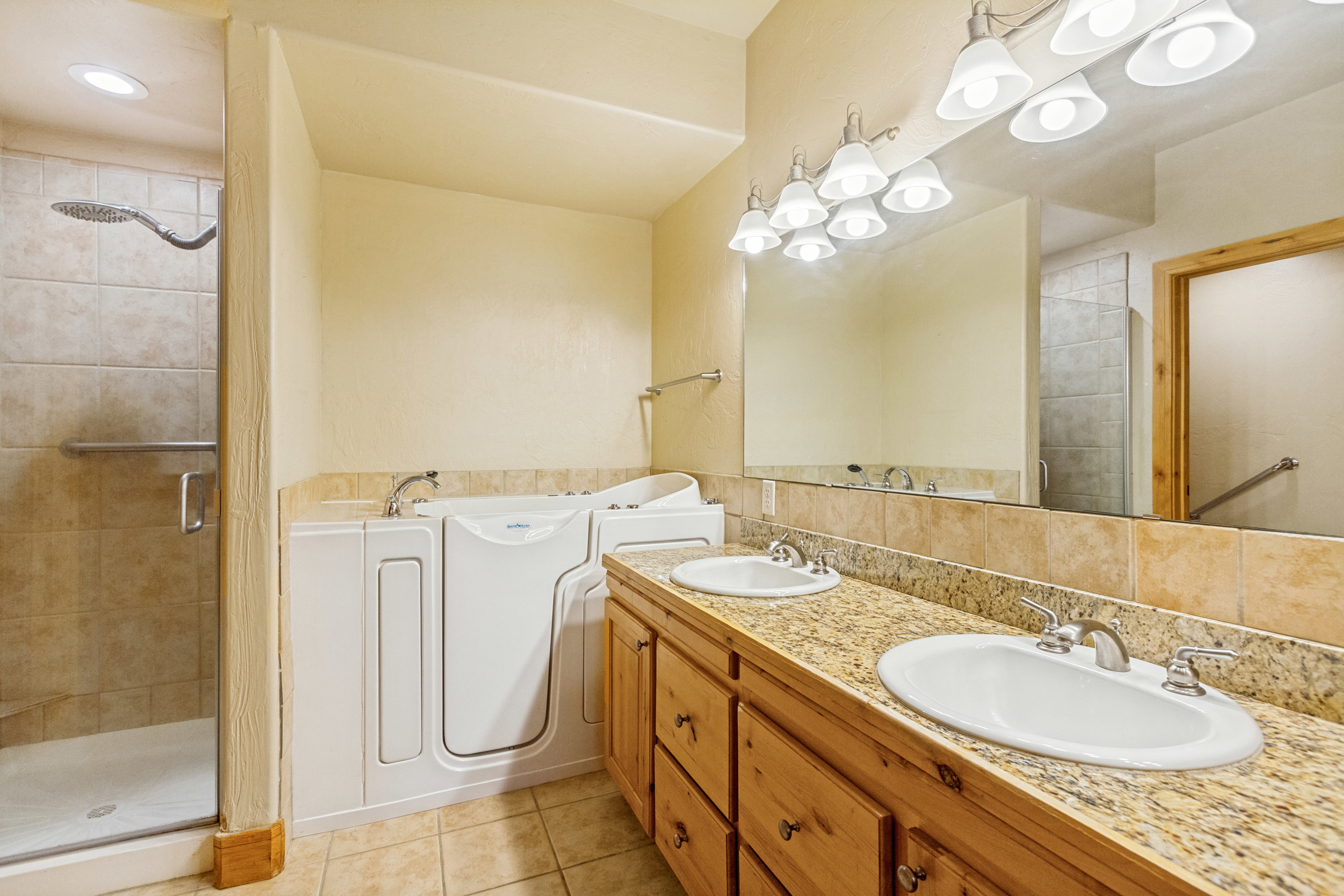 Bathroom featuring a walk-in tub, separate shower with glass enclosure, dual vanity with granite countertop, and wood-finish cabinetry