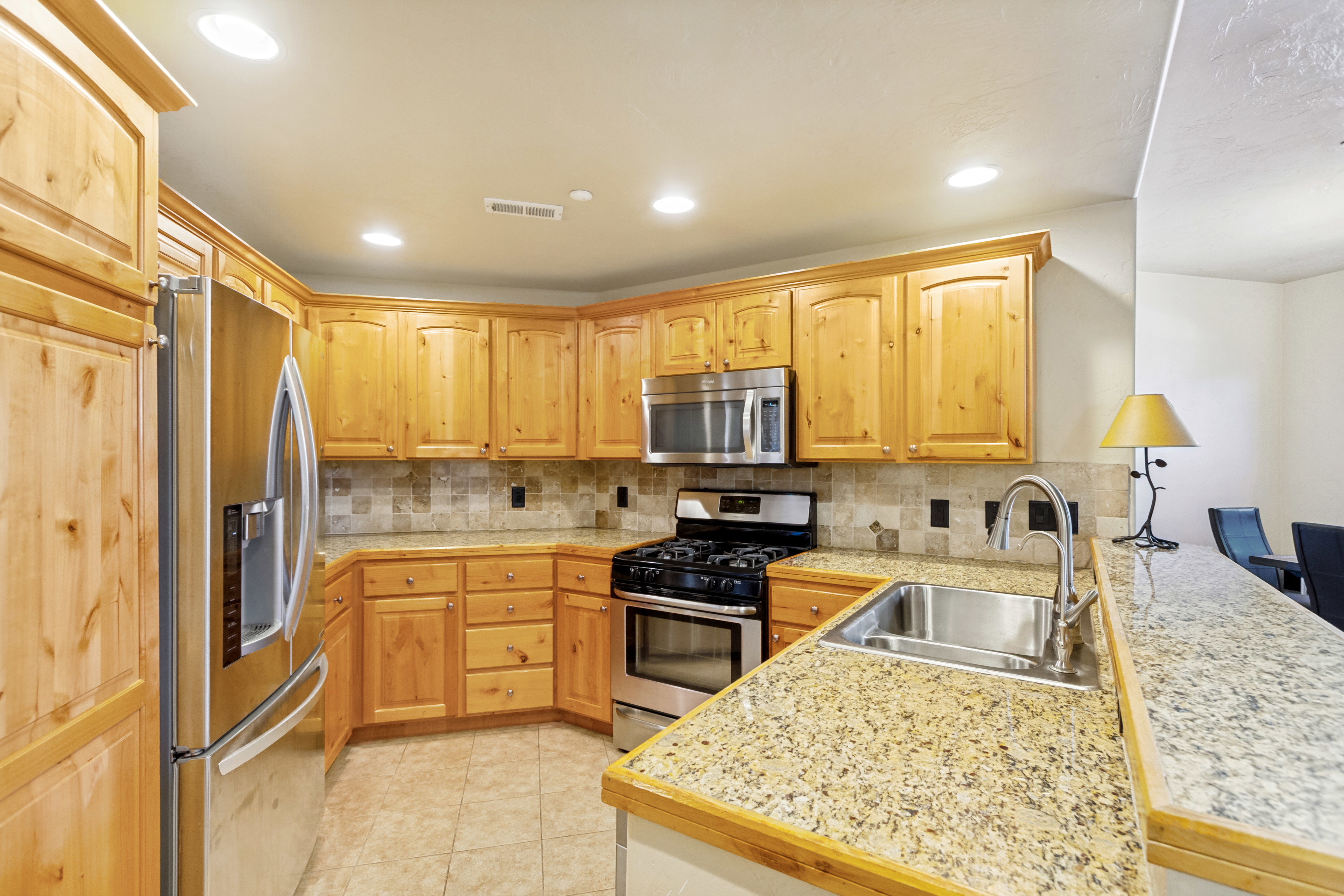 Kitchen featuring wood cabinetry, stainless steel appliances, speckled countertops, tile backsplash, and recessed lighting